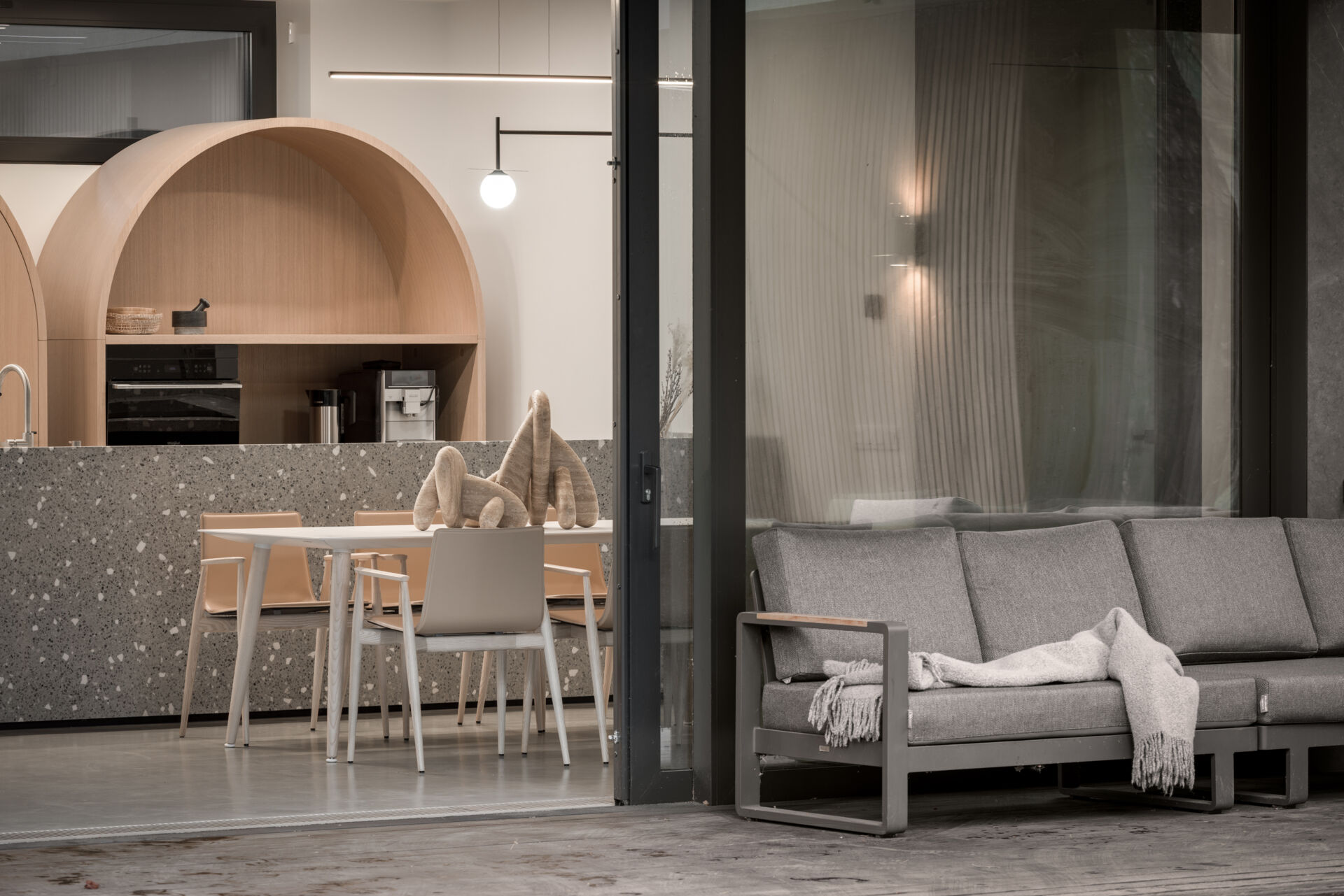 The terrace extends straight into the forest and acts as an outdoor continuation of the living area. It includes a lounge zone with a large sofa, an outdoor dining setup, and a summer kitchen with a grill.