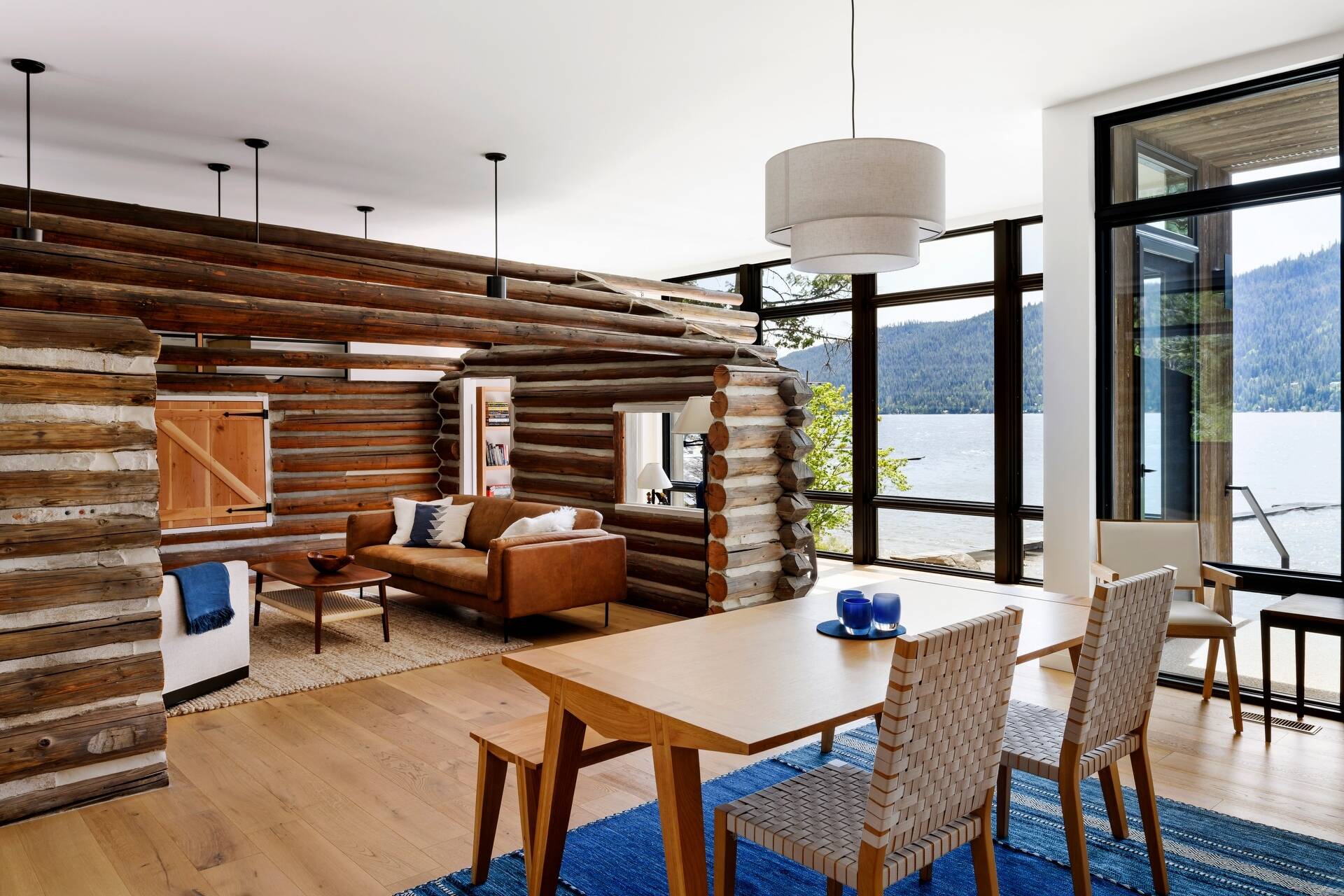 The restored log cabin now serves as the living room, complete with original materials and subtle modern lighting. Minimal interiors surround the cabin, balancing rugged textures with Scandinavian-inspired simplicity.