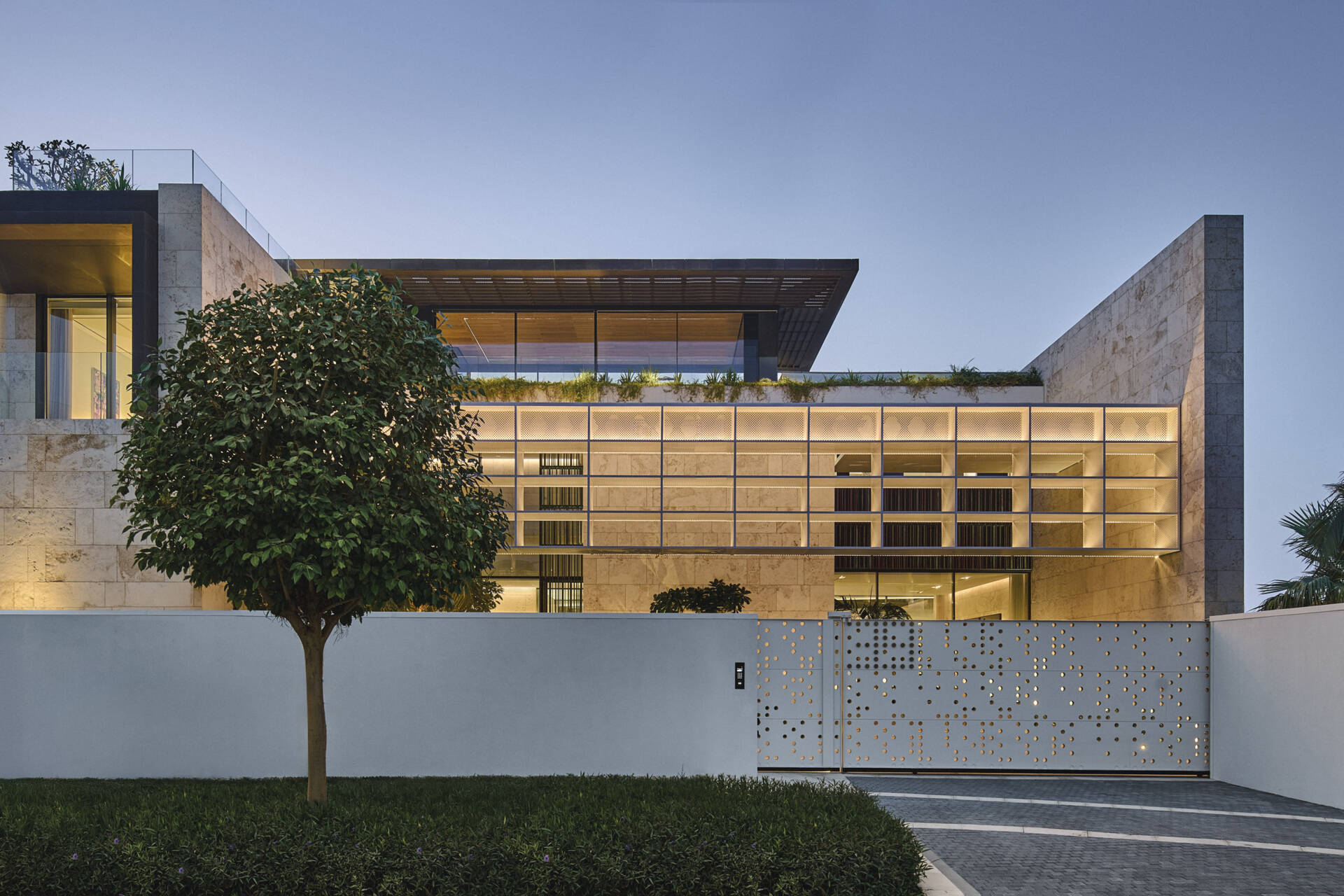 The sculptural street facade of Island Villa pairs coral textured stone with bespoke screens inspired by box kites. Deep overhangs and articulated rooflines shape a grounded yet porous presence designed for privacy and climate responsiveness.