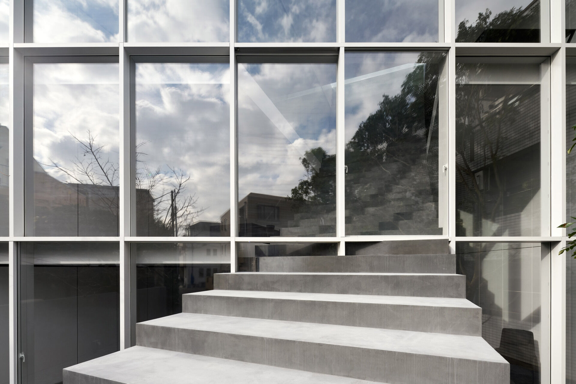 A minimalist Tokyo home where a single staircase starts in the garden, continues indoors, and rises toward a skylight, turning everyday movement into the home’s most striking architectural feature.