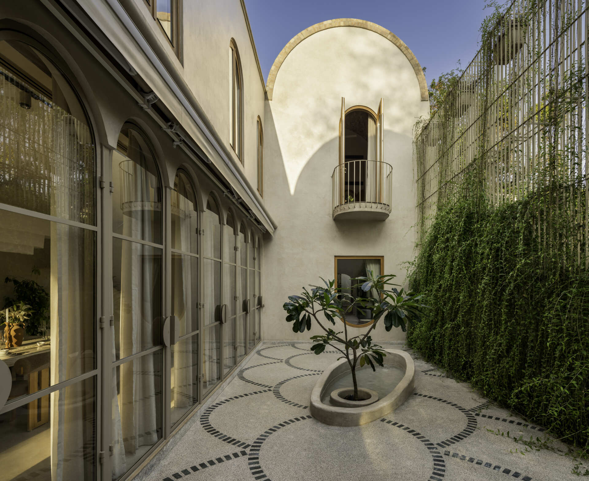 At the heart of the house, a courtyard with green marble terrazzo flooring and an elliptical sit-out wraps around a tree, reinterpreting traditional Goan balcão seating.