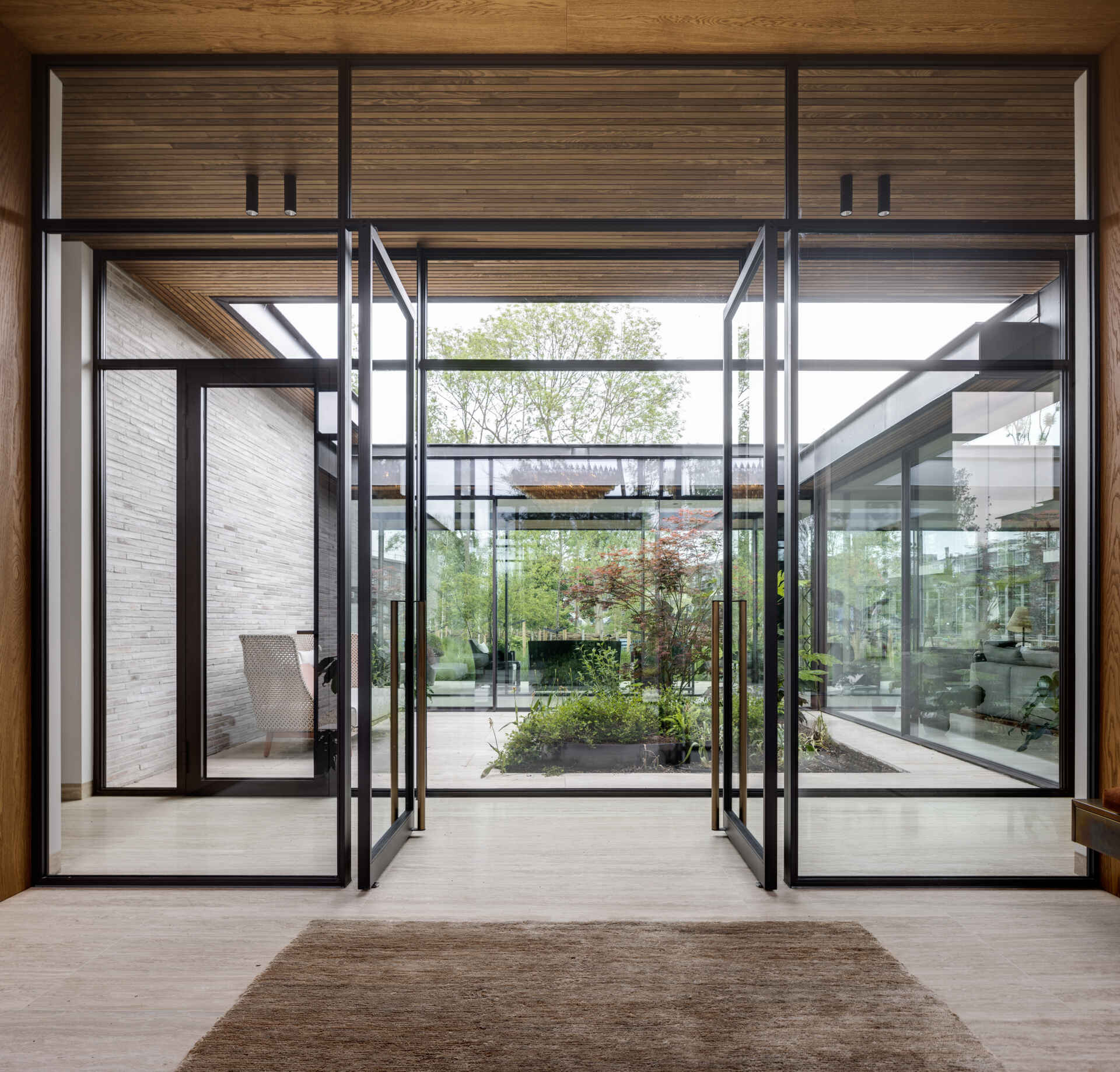 At the center of the house, the patio defines both circulation and atmosphere. A glazed corridor passes around it, forming a clear axis that links spaces while allowing light and air to move freely. From multiple rooms, the eye returns to greenery.