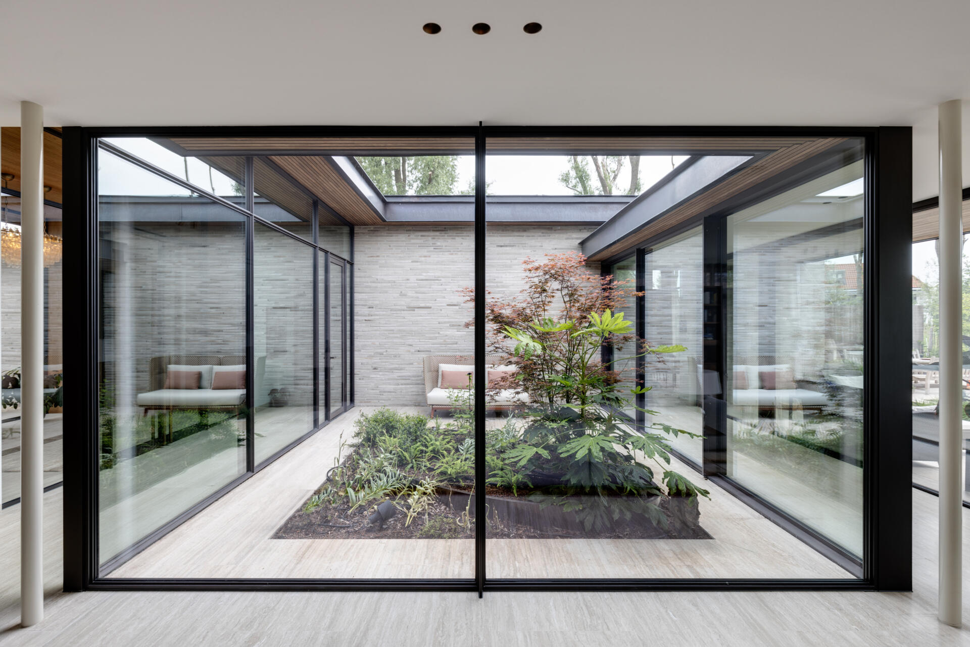 At the center of the house, the patio defines both circulation and atmosphere. A glazed corridor passes around it, forming a clear axis that links spaces while allowing light and air to move freely. From multiple rooms, the eye returns to greenery.