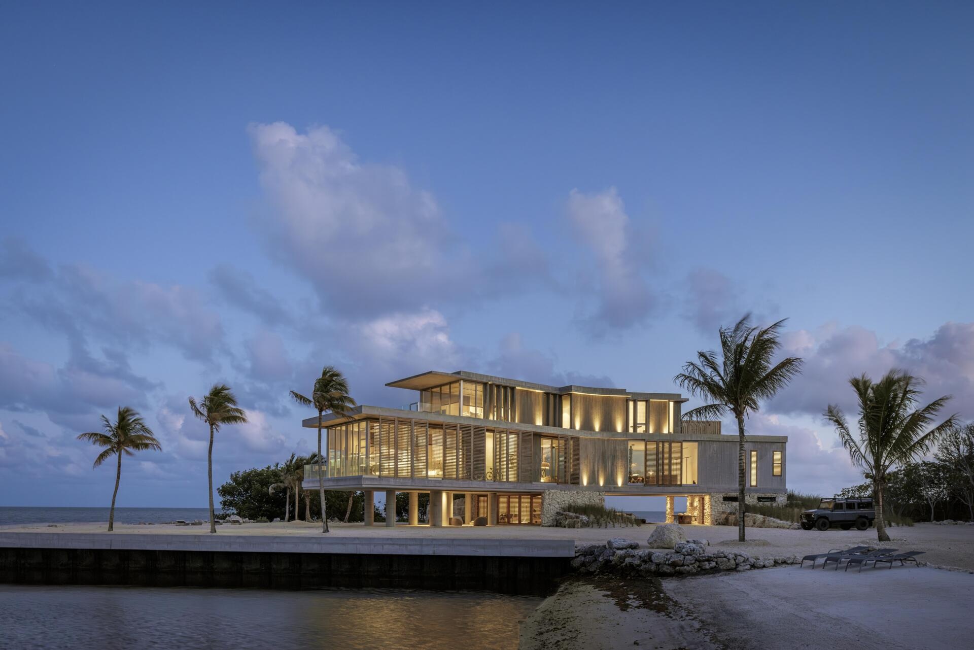 This modern home features board-formed concrete, coral rock, and wood slats that define a durable material palette built for coastal conditions.