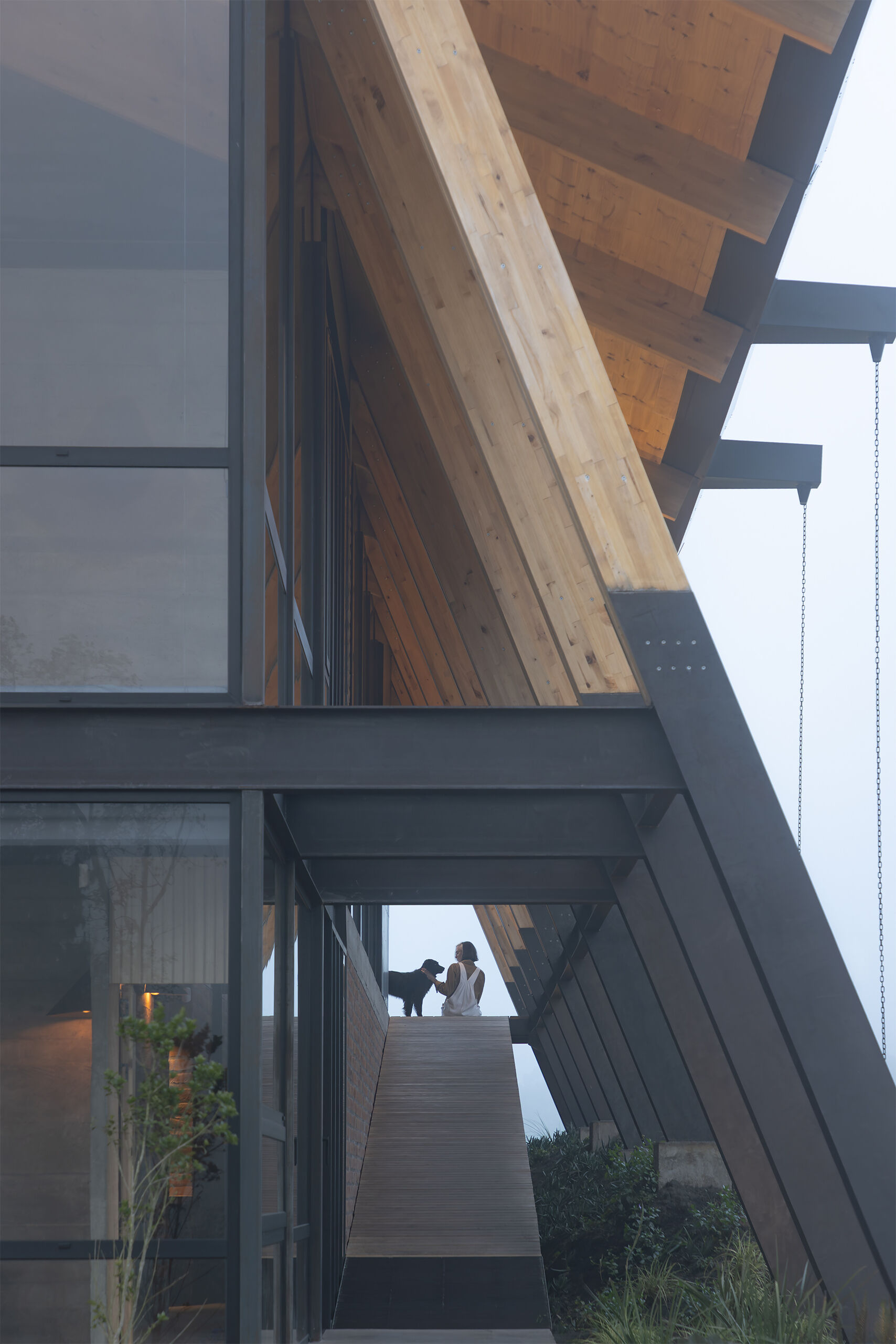 Ten wooden ribs define the rhythm of this Ecuadorian home. Large eaves, a brick base, and a covered ramp shape how the house meets the slope and protects against sun and rain.