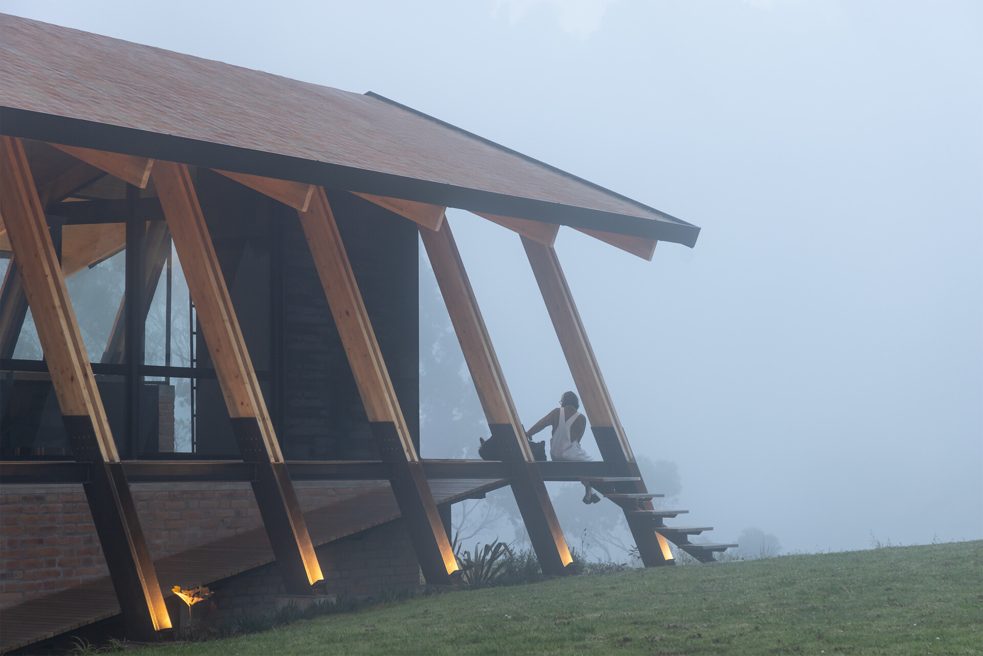 Ten wooden ribs define the rhythm of this Ecuadorian home. Large eaves, a brick base, and a covered ramp shape how the house meets the slope and protects against sun and rain.