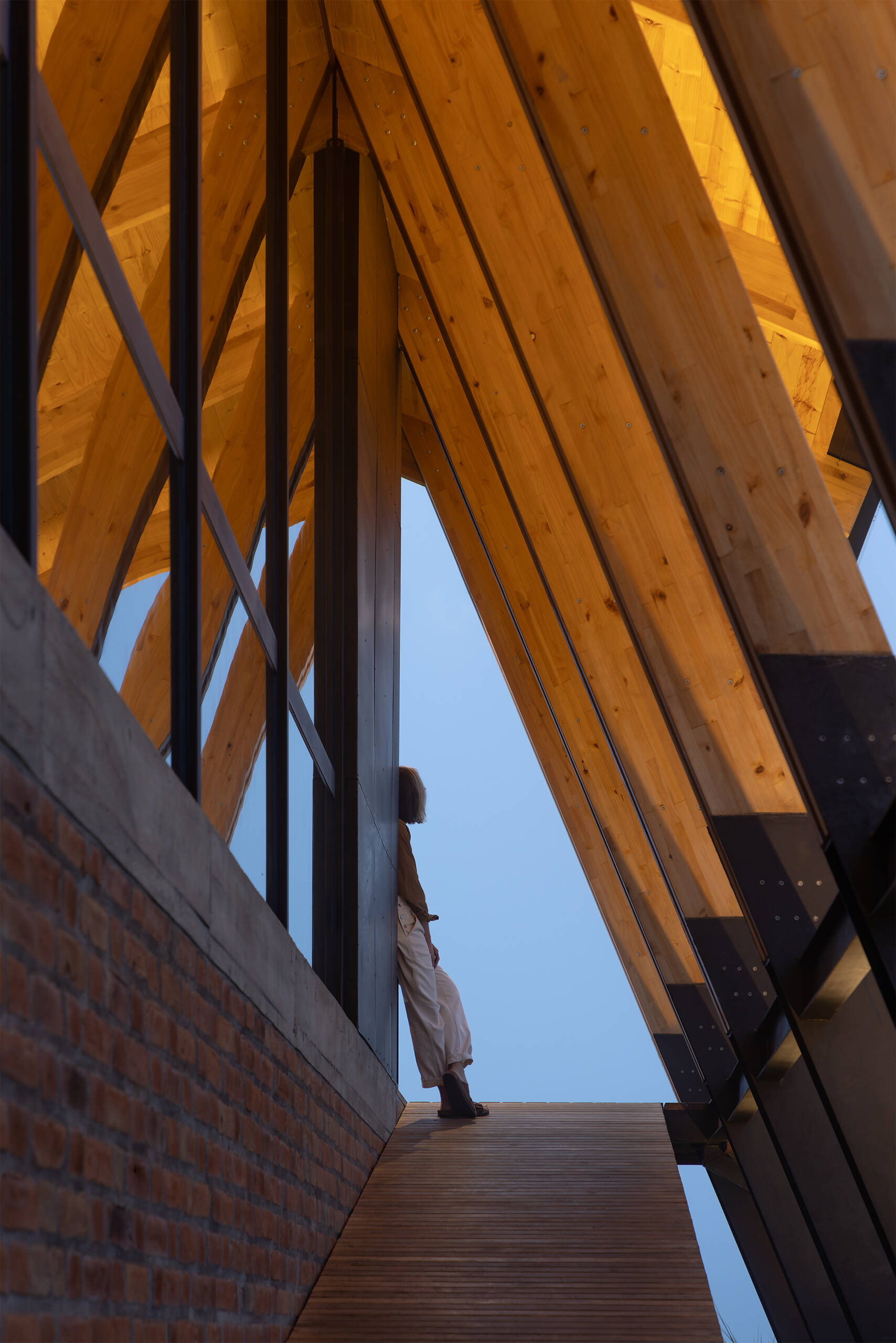 Ten wooden ribs define the rhythm of this Ecuadorian home. Large eaves, a brick base, and a covered ramp shape how the house meets the slope and protects against sun and rain.