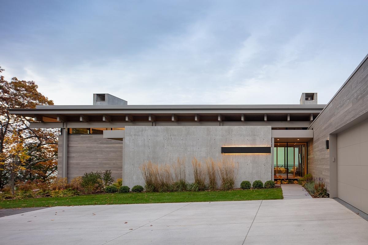 The entryway is hidden behind a concrete wall, guiding visitors through the four-season room to stunning lake views. The driveway and garage maintain privacy while creating a welcoming approach.