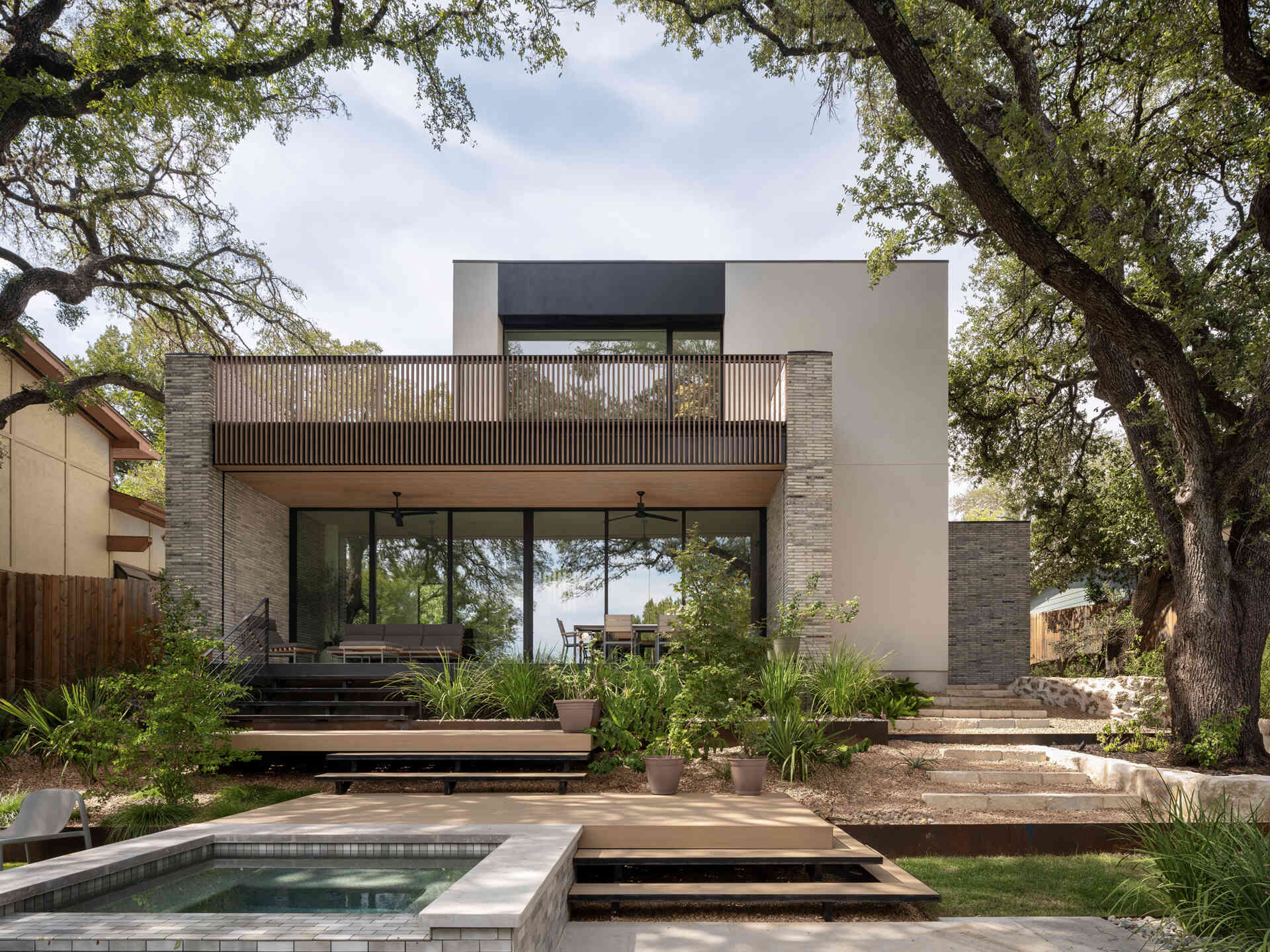 Terraced platforms descend toward a private pool, turning a hillside lot into an asset. Layered outdoor spaces preserve privacy while framing long views over the tree canopy and beyond.