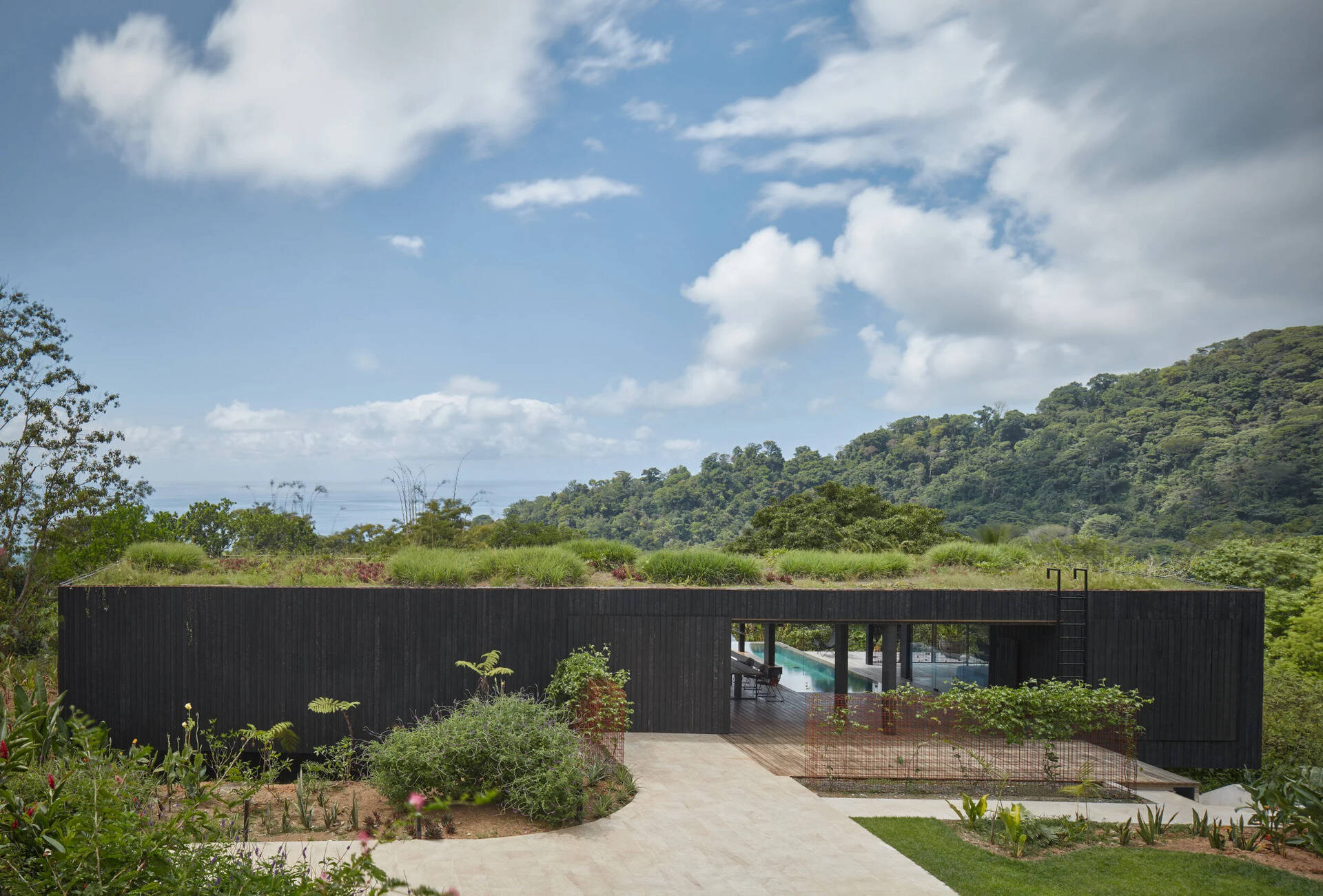 This windowless burnt teak façade creates total privacy from the driveway, hiding a light filled tropical retreat behind dark, charred wood.