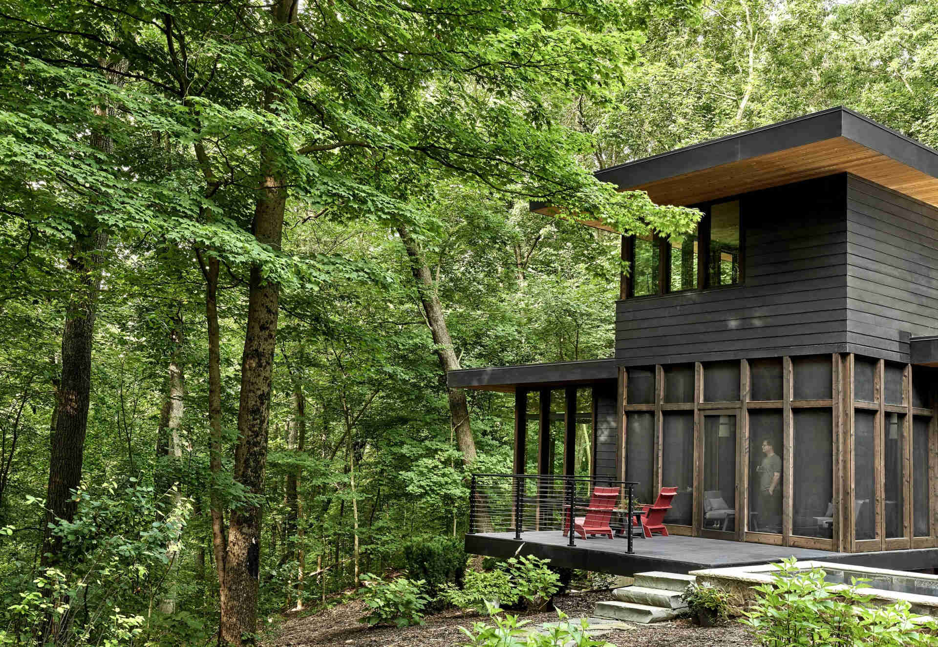 A shaded sunroom opens to a patio and garden, creating an easy flow between indoor comfort and the surrounding woods.