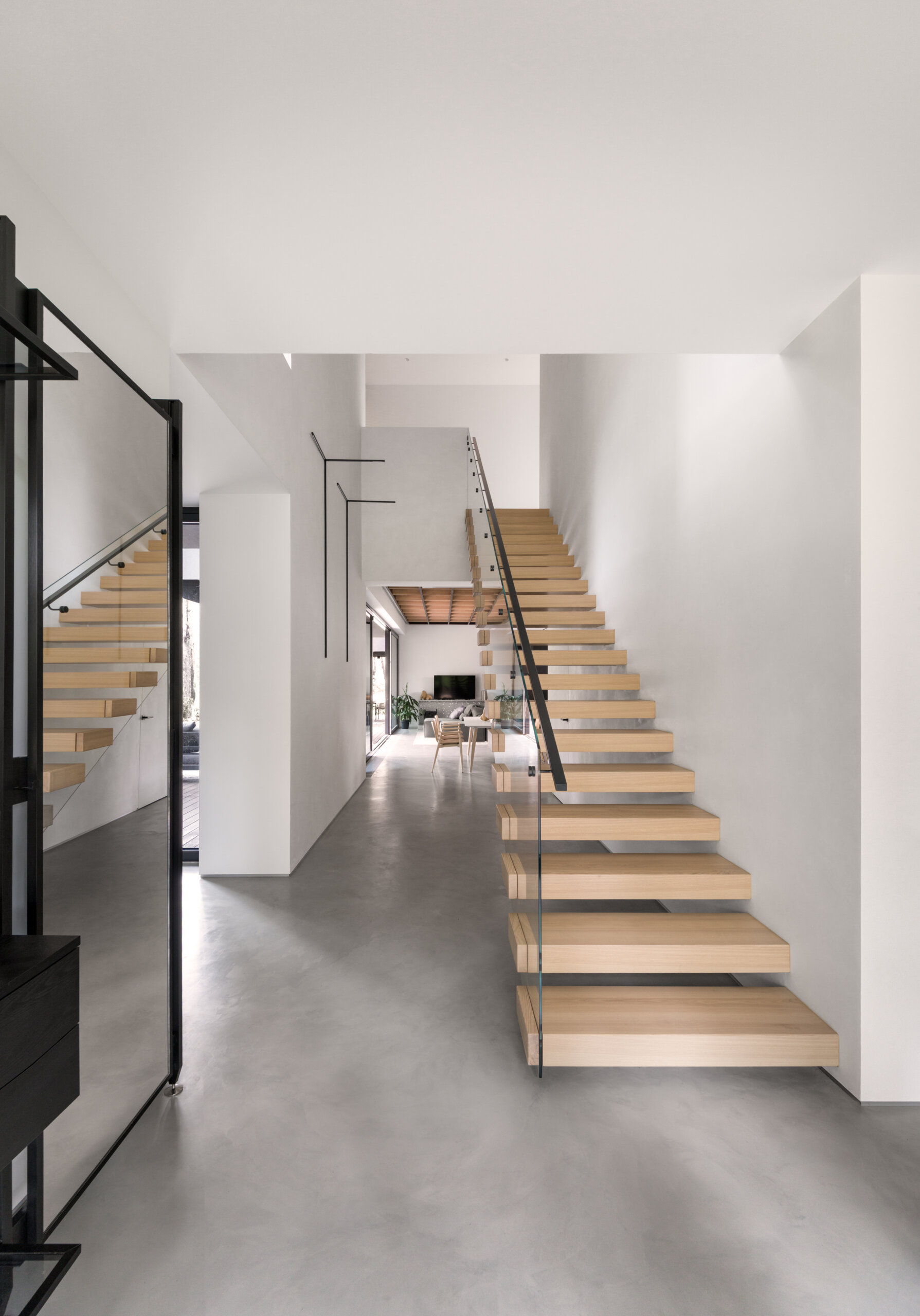 The wood staircase connects the shared ground floor to the more private upper level. It functions as a transition between social and quiet zones within the house. Light and material choices keep the movement between floors calm and understated.