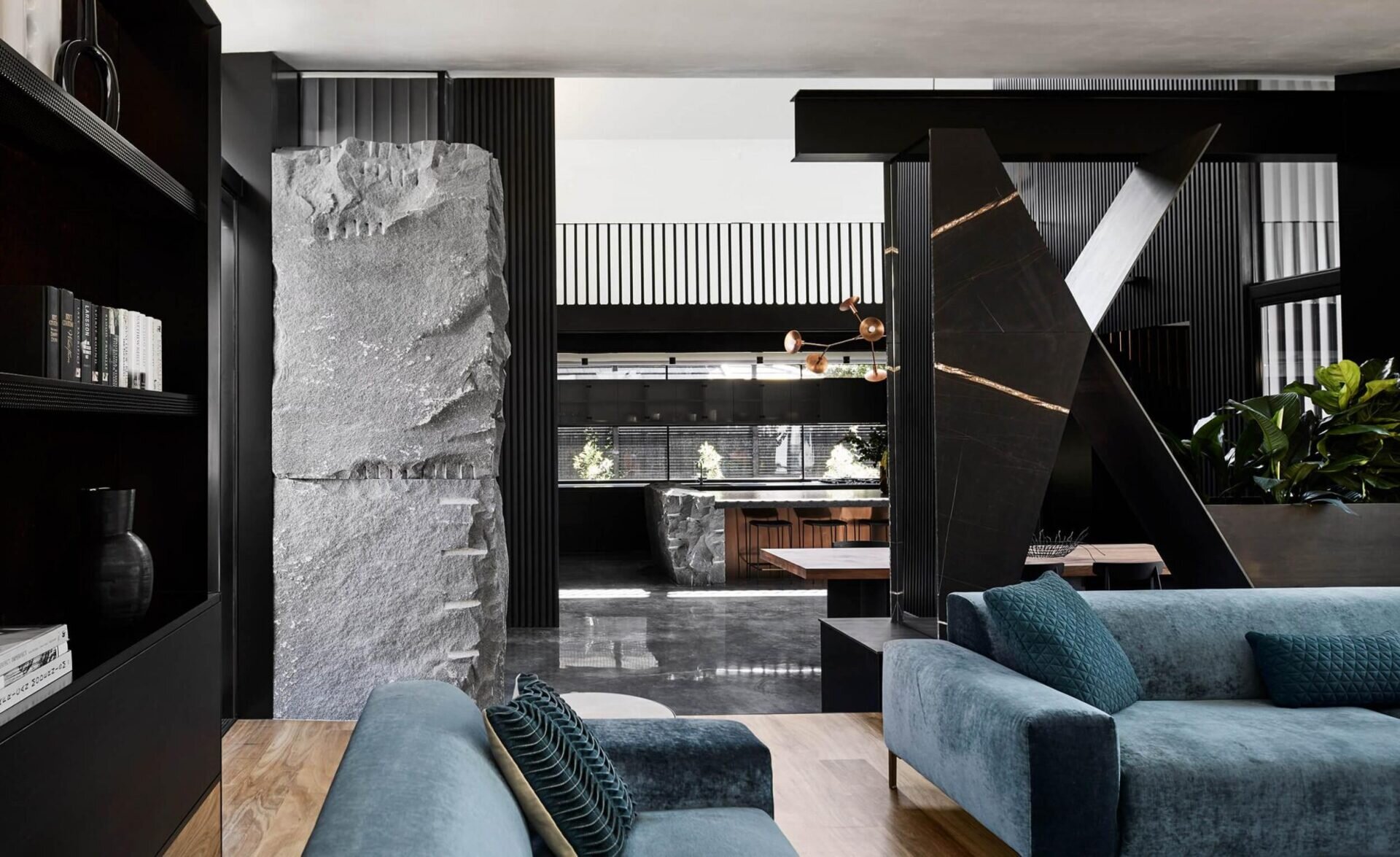 Colorful soft furnishings and a dramatic fireplace hearth soften the stone and steel elements. The living room connects seamlessly to the outdoors through expansive glass doors.