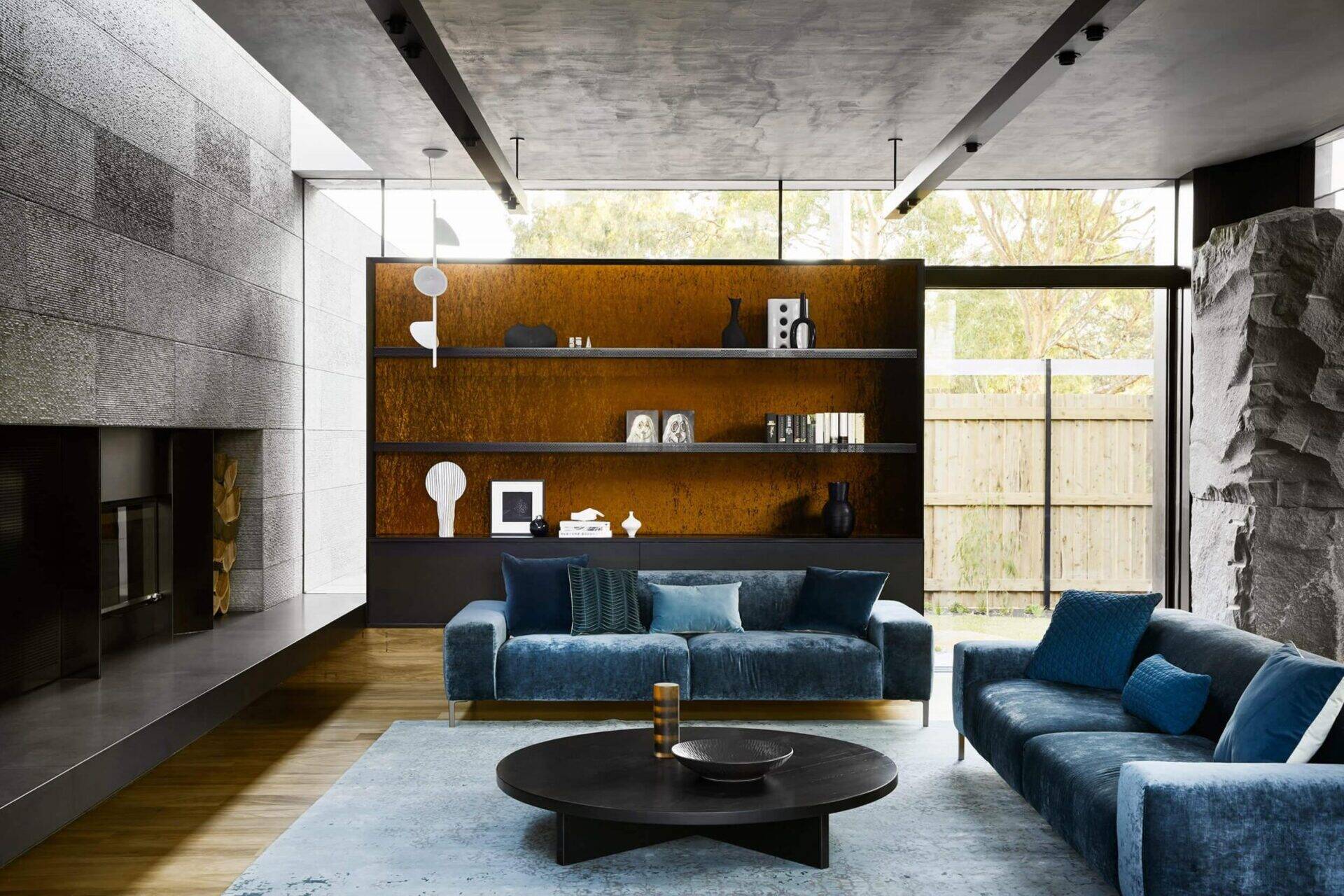 Colorful soft furnishings and a dramatic fireplace hearth soften the stone and steel elements. The living room connects seamlessly to the outdoors through expansive glass doors.