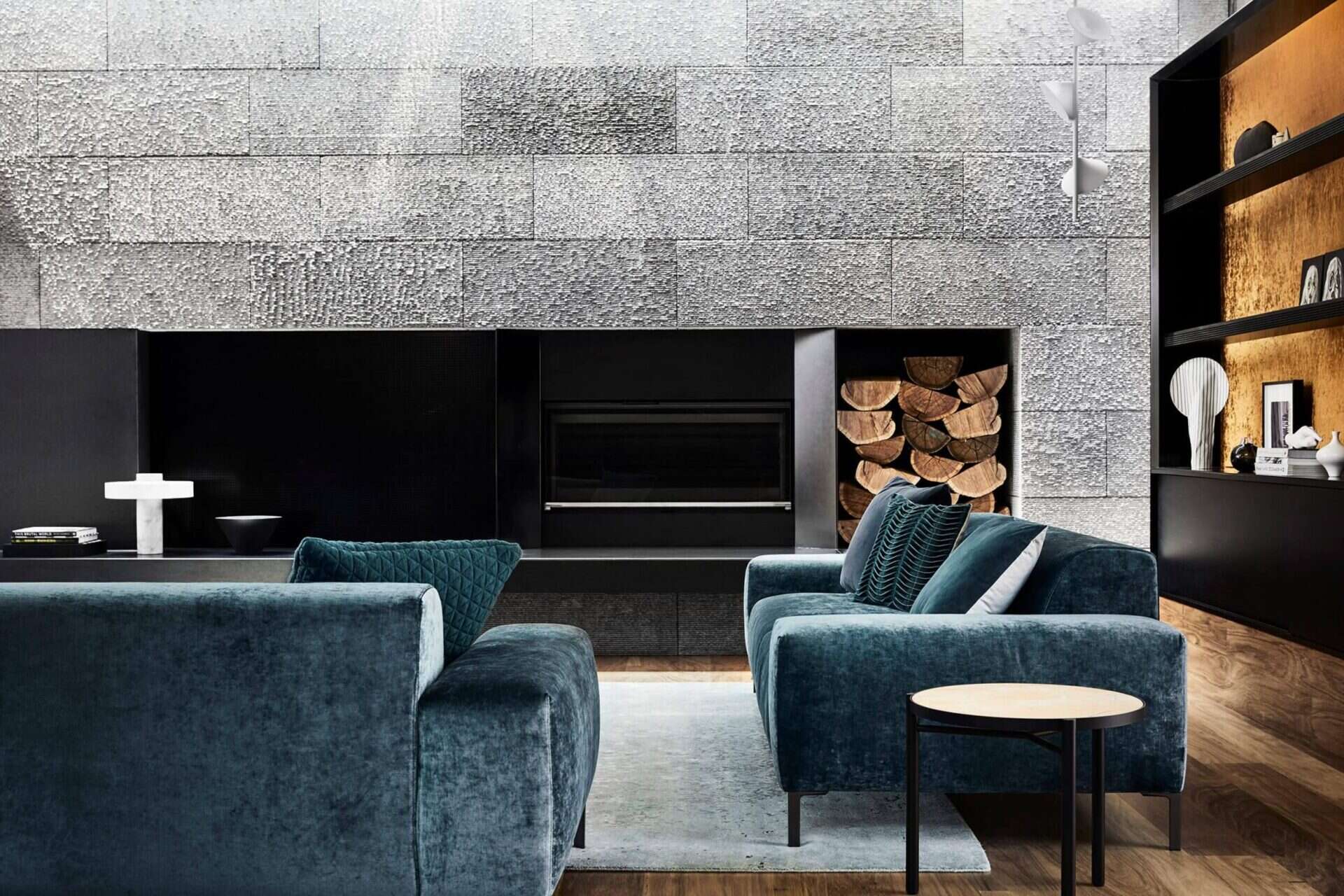 Colorful soft furnishings and a dramatic fireplace hearth soften the stone and steel elements. The living room connects seamlessly to the outdoors through expansive glass doors.
