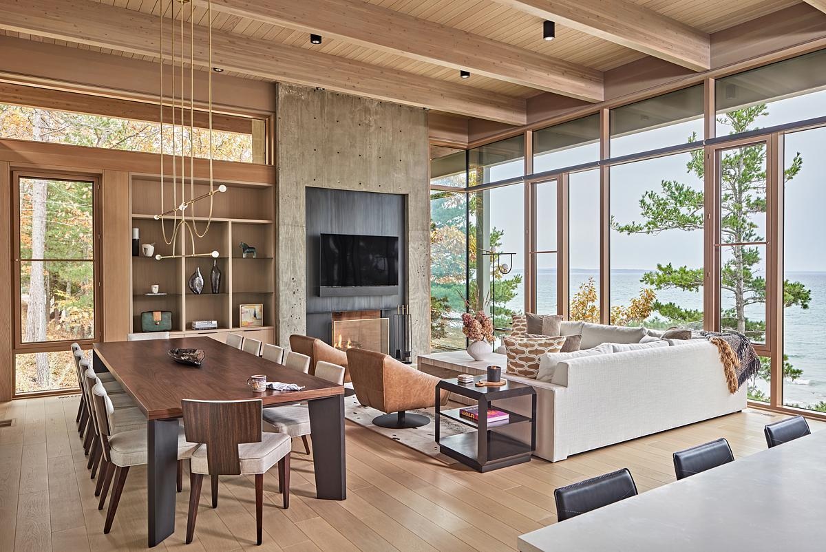 The living and dining areas feature floor-to-ceiling window walls, bringing natural light and panoramic lake views into the home. A monolithic concrete fireplace anchors the open yet intimate space.