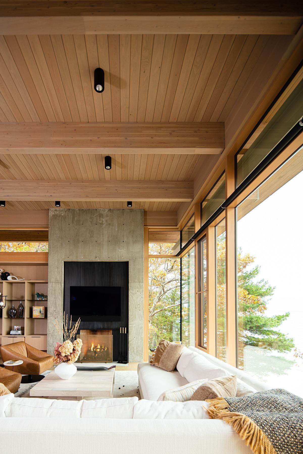 The living and dining areas feature floor-to-ceiling window walls, bringing natural light and panoramic lake views into the home. A monolithic concrete fireplace anchors the open yet intimate space.