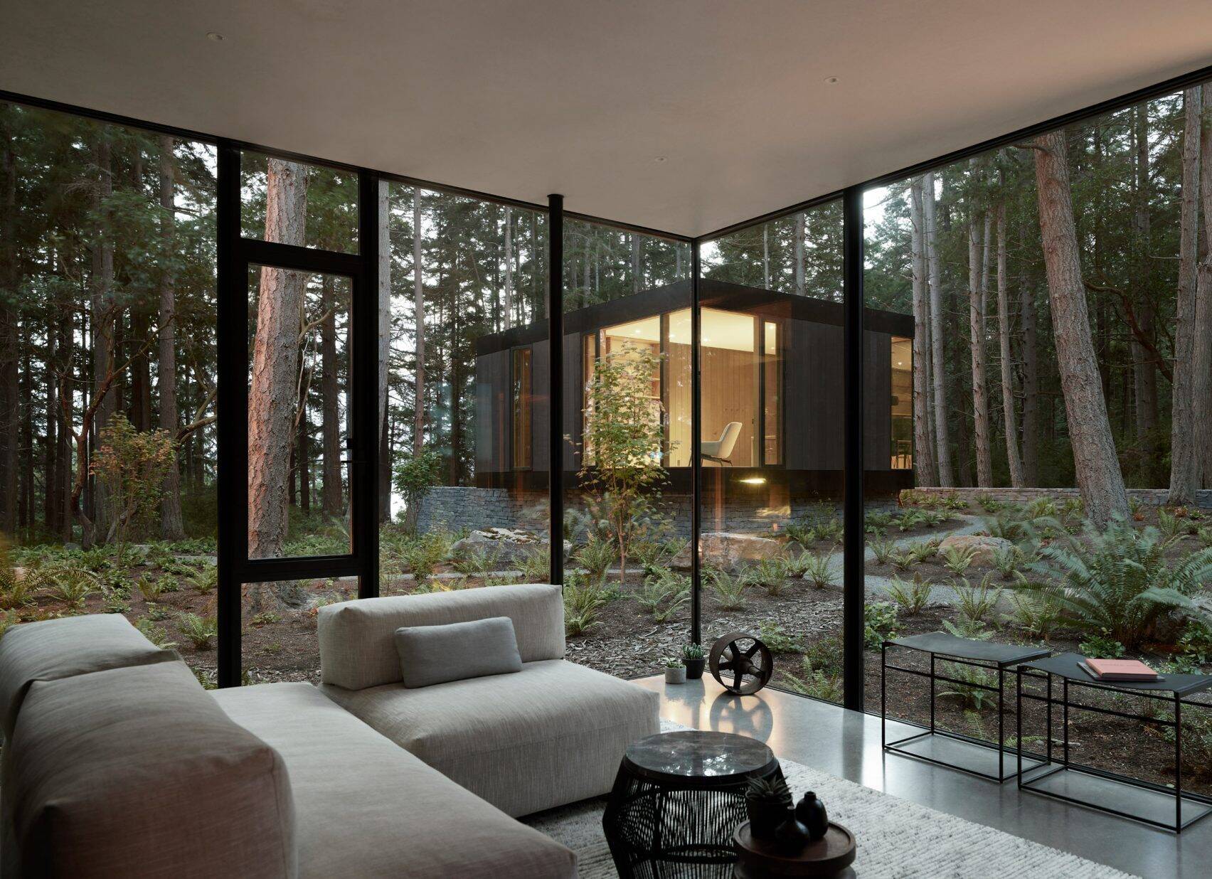 Beyond the main living area is a secondary lounge defined by a dark wood wall. From here, there are views toward another structure that stands apart from the primary house.