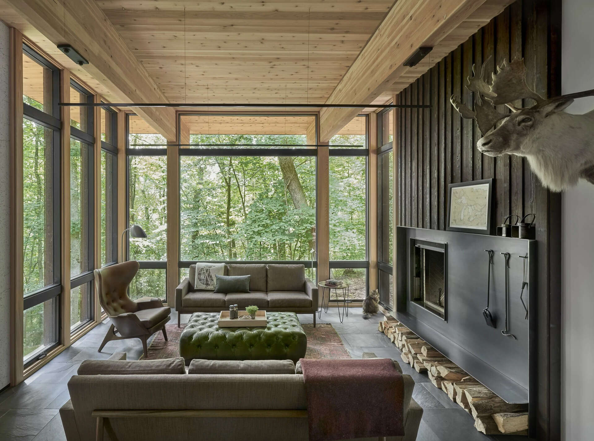 A charred cedar accent wall and blackened steel fireplace create a dramatic focal point against a backdrop of forest views.