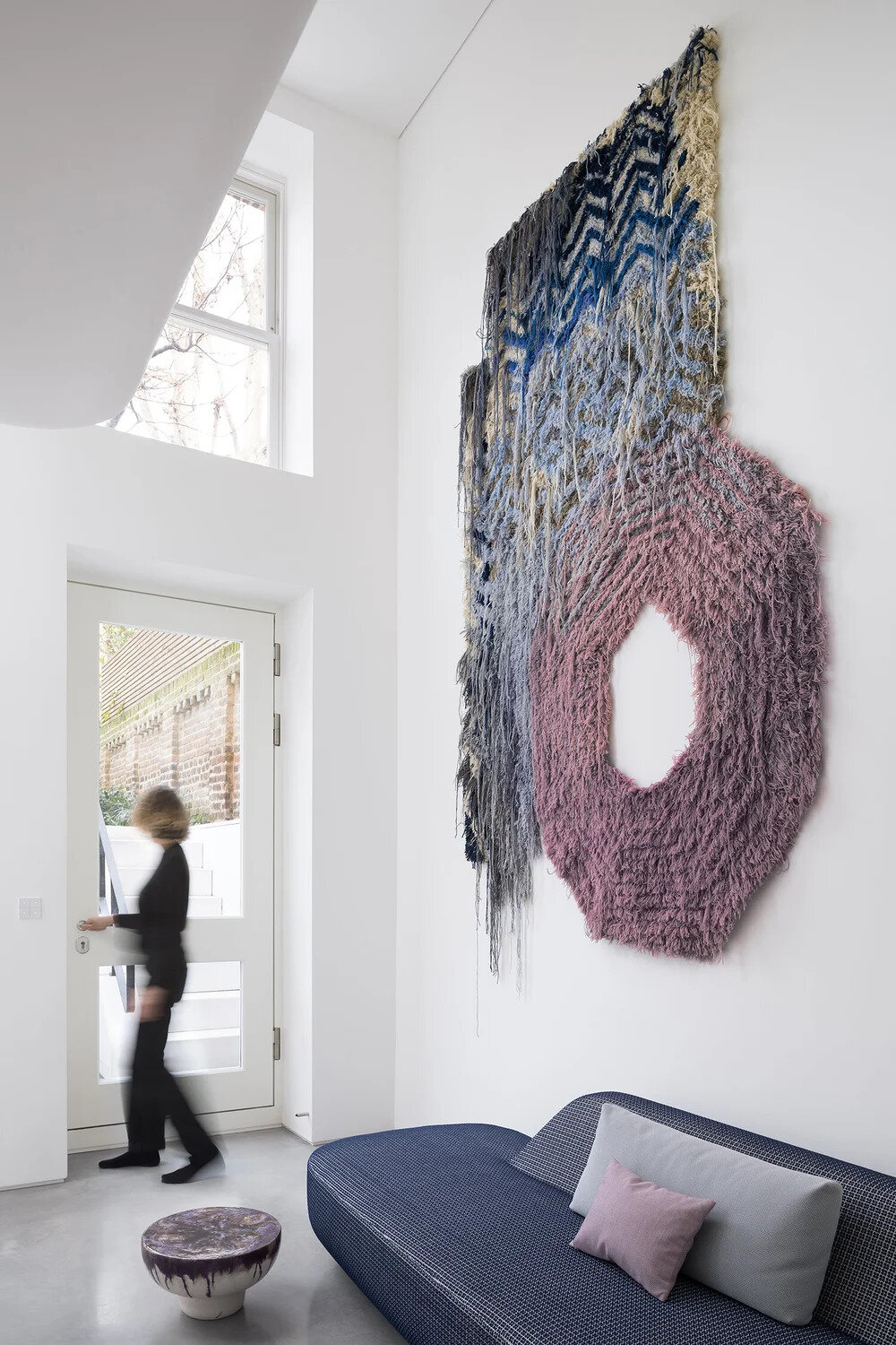 A soaring double height living room features a woven textile artwork and visual connections to the upper floors.