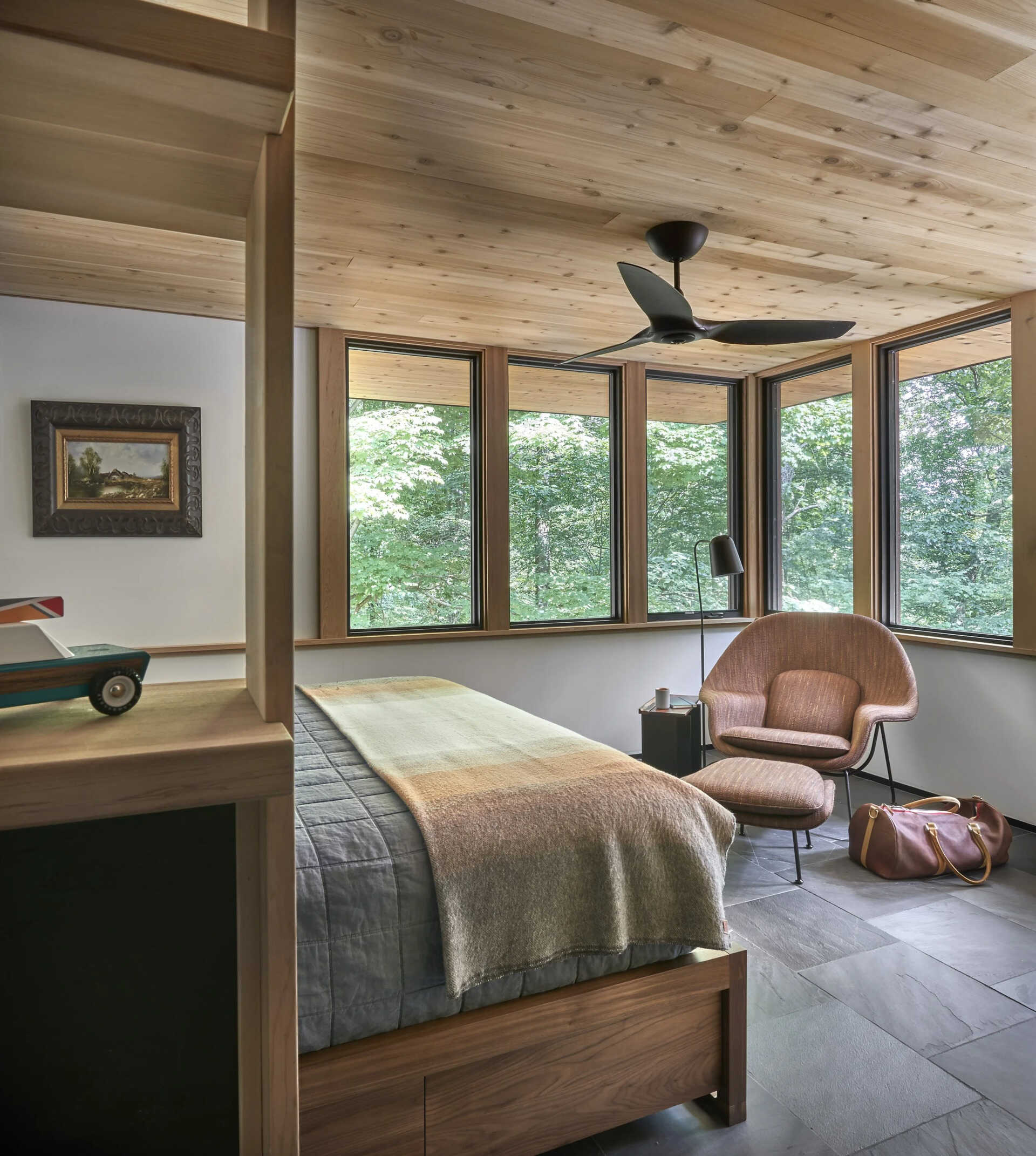 Corner windows fill the bedroom with natural light and uninterrupted views of the surrounding trees.