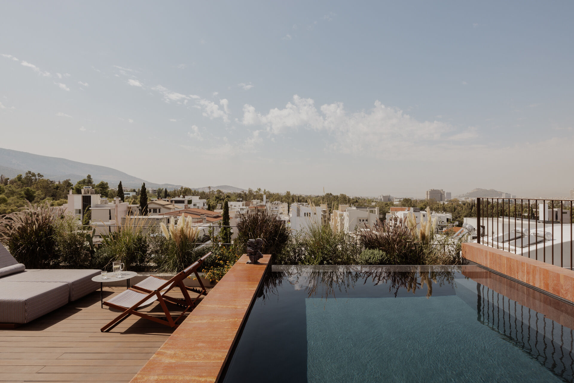 A south facing roof terrace in Papagou featuring a swimming pool, deck and half size basketball court surrounded by greenery.