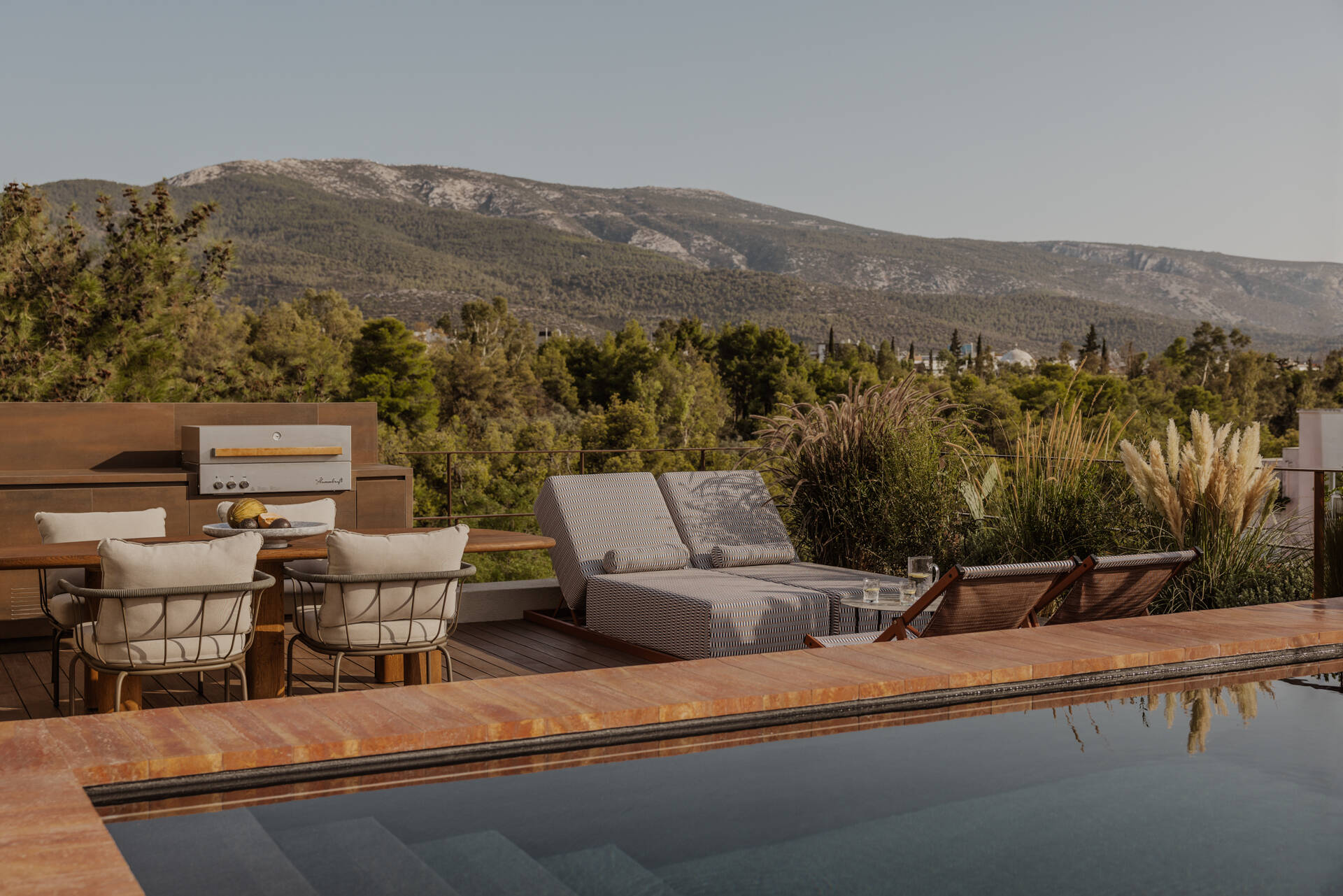 A south facing roof terrace in Papagou featuring a swimming pool, deck and half size basketball court surrounded by greenery.