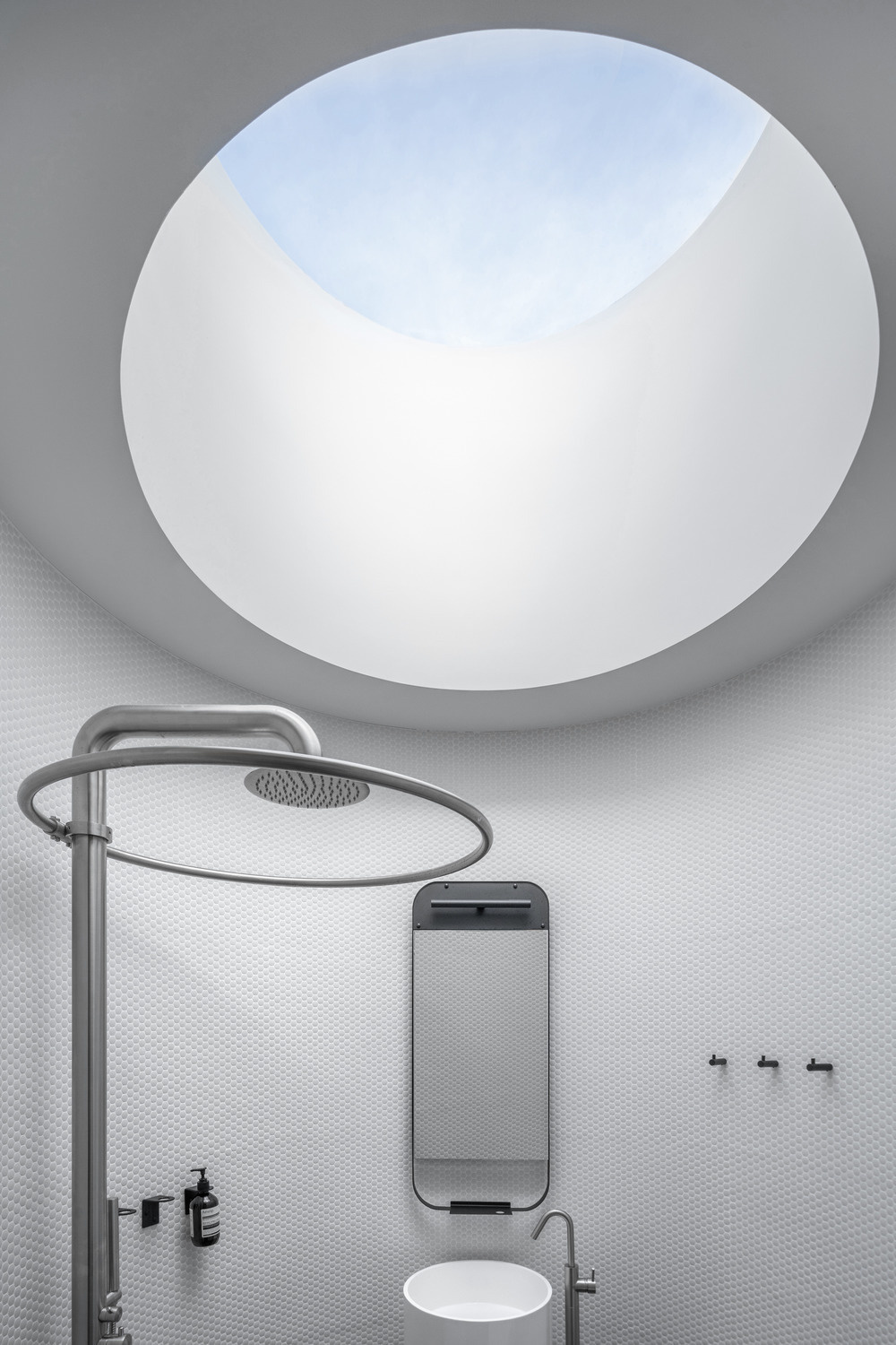 A cylindrical bathroom clad in red cedar stands as a warm sculptural feature within the glass pool house, complete with a curved bench and hidden entrance.