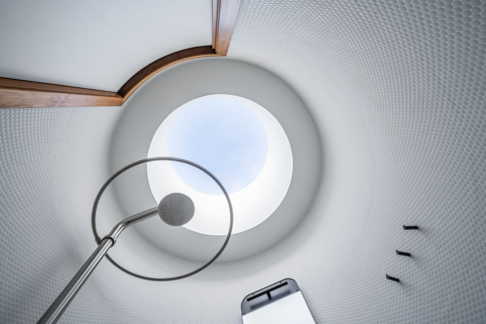A cylindrical bathroom clad in red cedar stands as a warm sculptural feature within the glass pool house, complete with a curved bench and hidden entrance.
