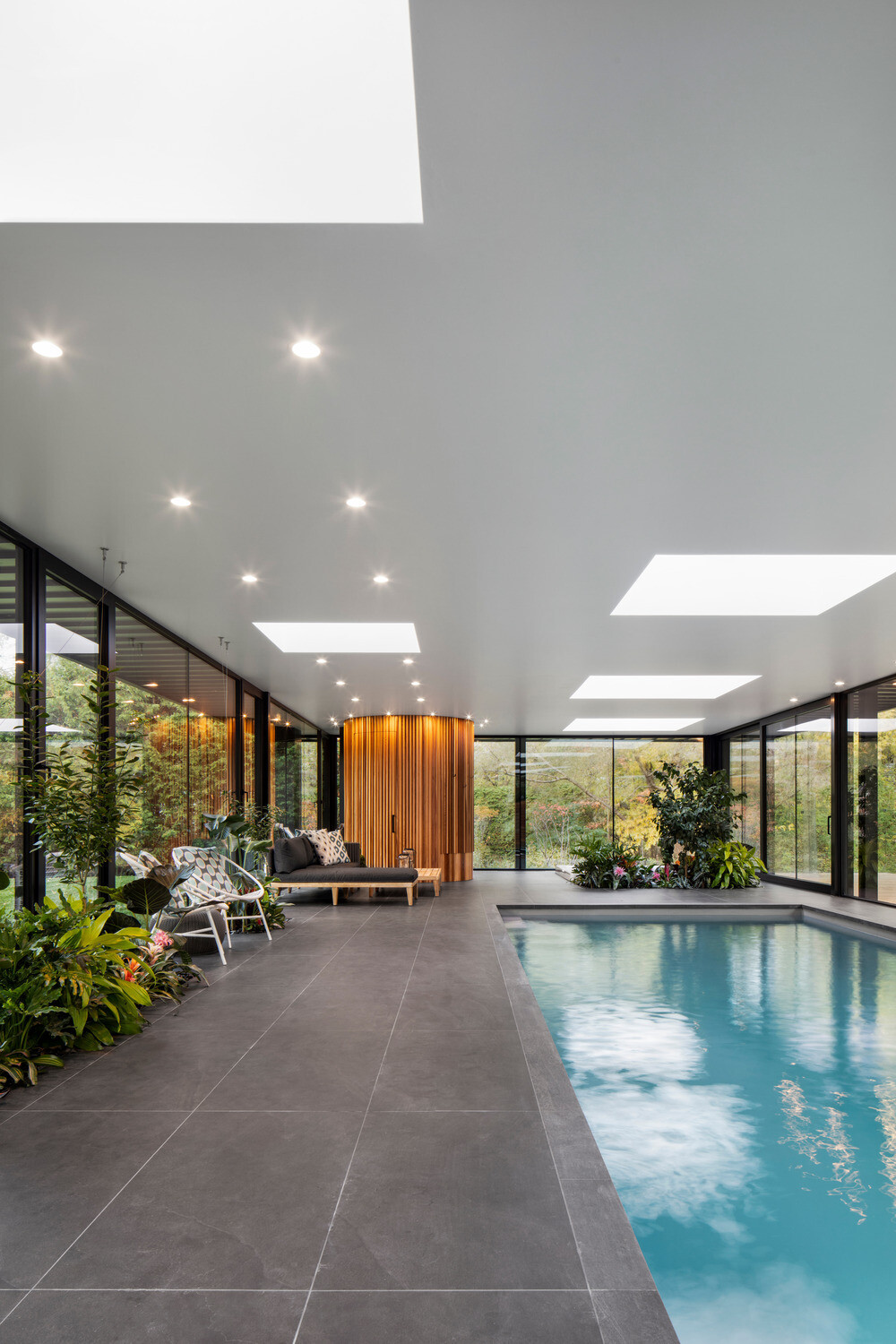 Skylights flood the interior with natural light while a lounging deck and layers of tropical plants create an oasis feel inside this modern glass pool house.