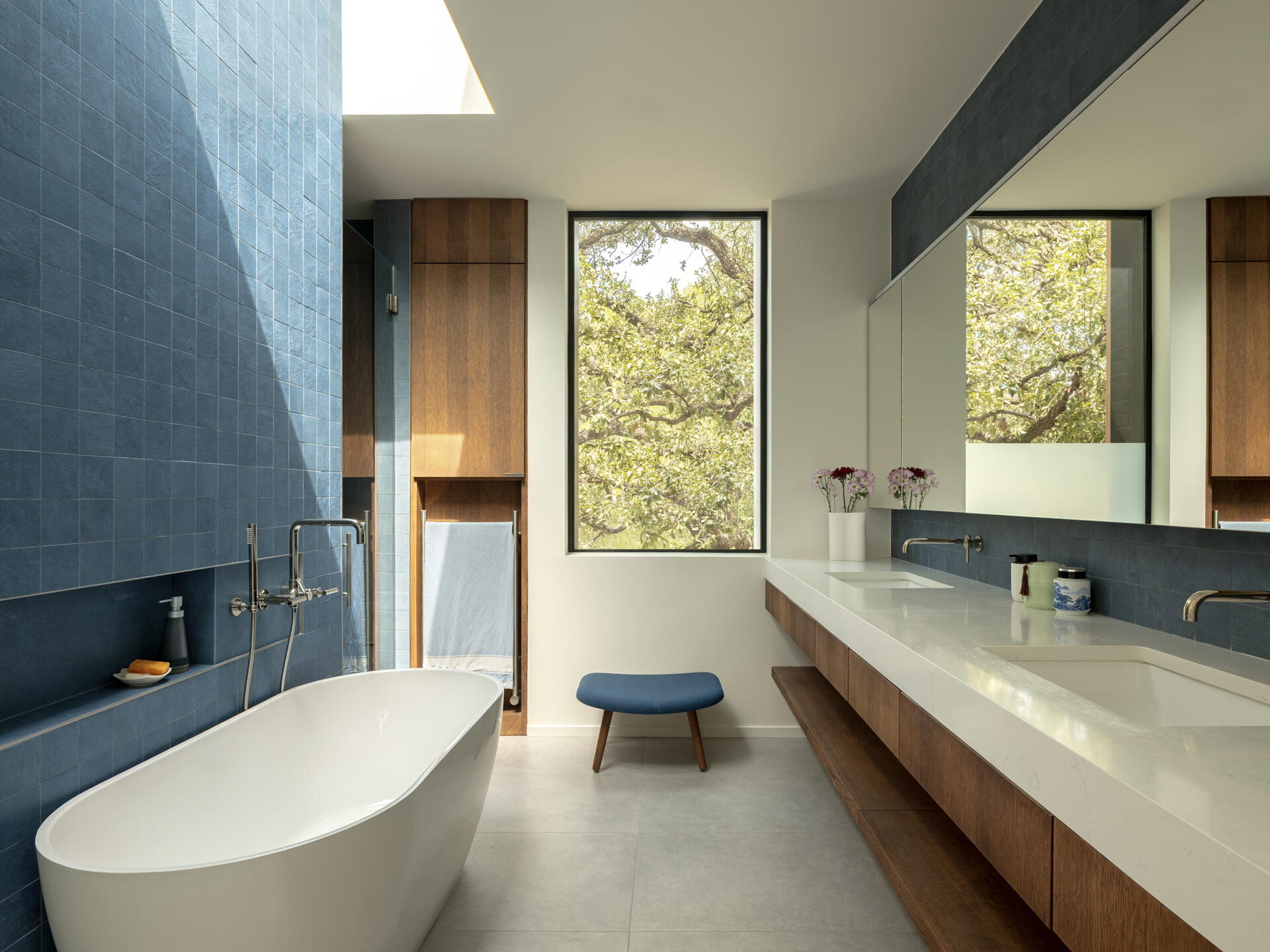 This modern ensuite bathroom features a square blue tile accent wall below a skylight, while a double vanity lines the opposite wall.