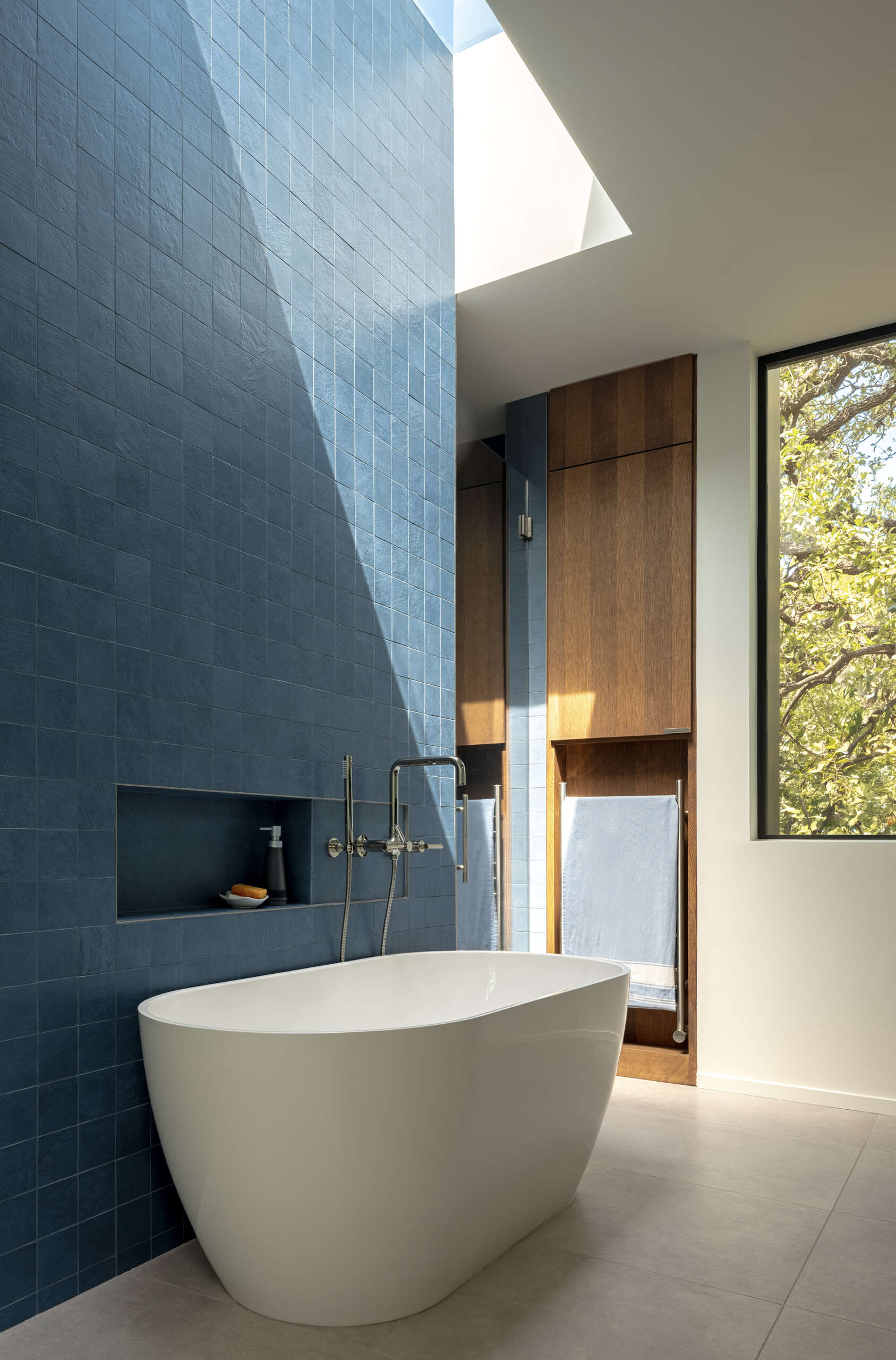 This modern ensuite bathroom features a square blue tile accent wall below a skylight, while a double vanity lines the opposite wall.
