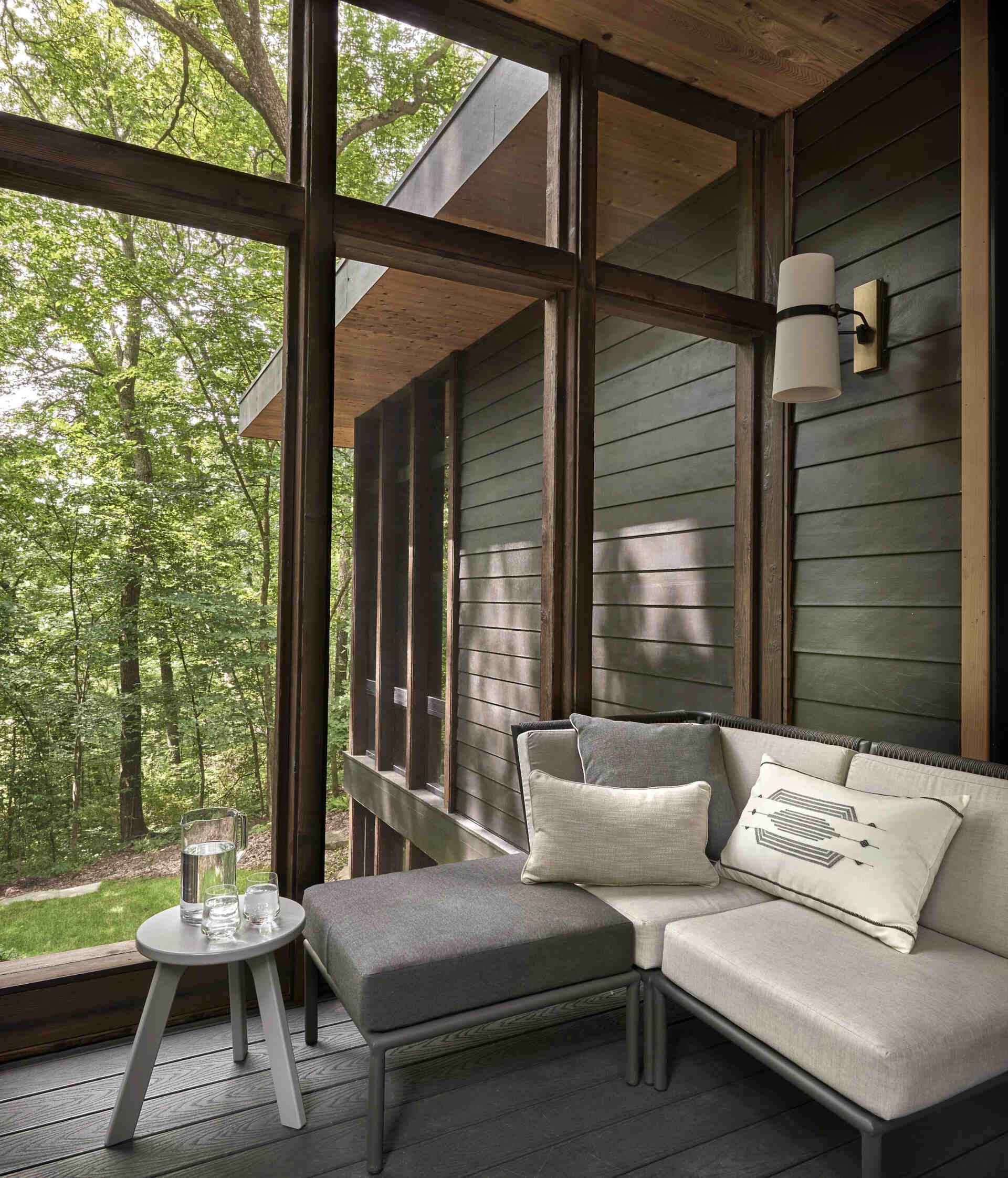 A shaded sunroom opens to a patio and garden, creating an easy flow between indoor comfort and the surrounding woods.