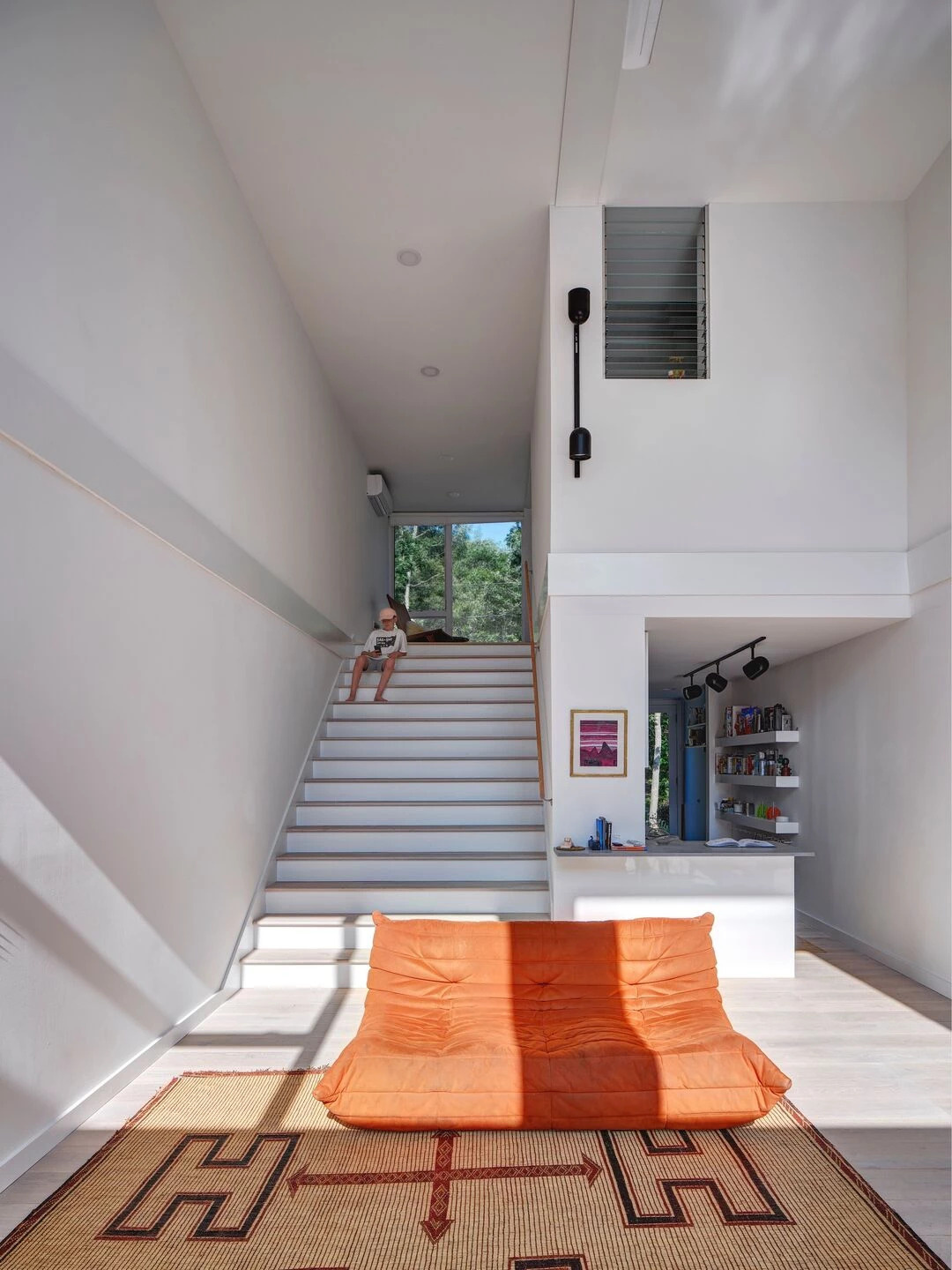 Black framed windows flood the interior with light, while large doors connect to outdoor seating areas and a swimming pool. Indoor and outdoor living blend seamlessly on this compact site.
