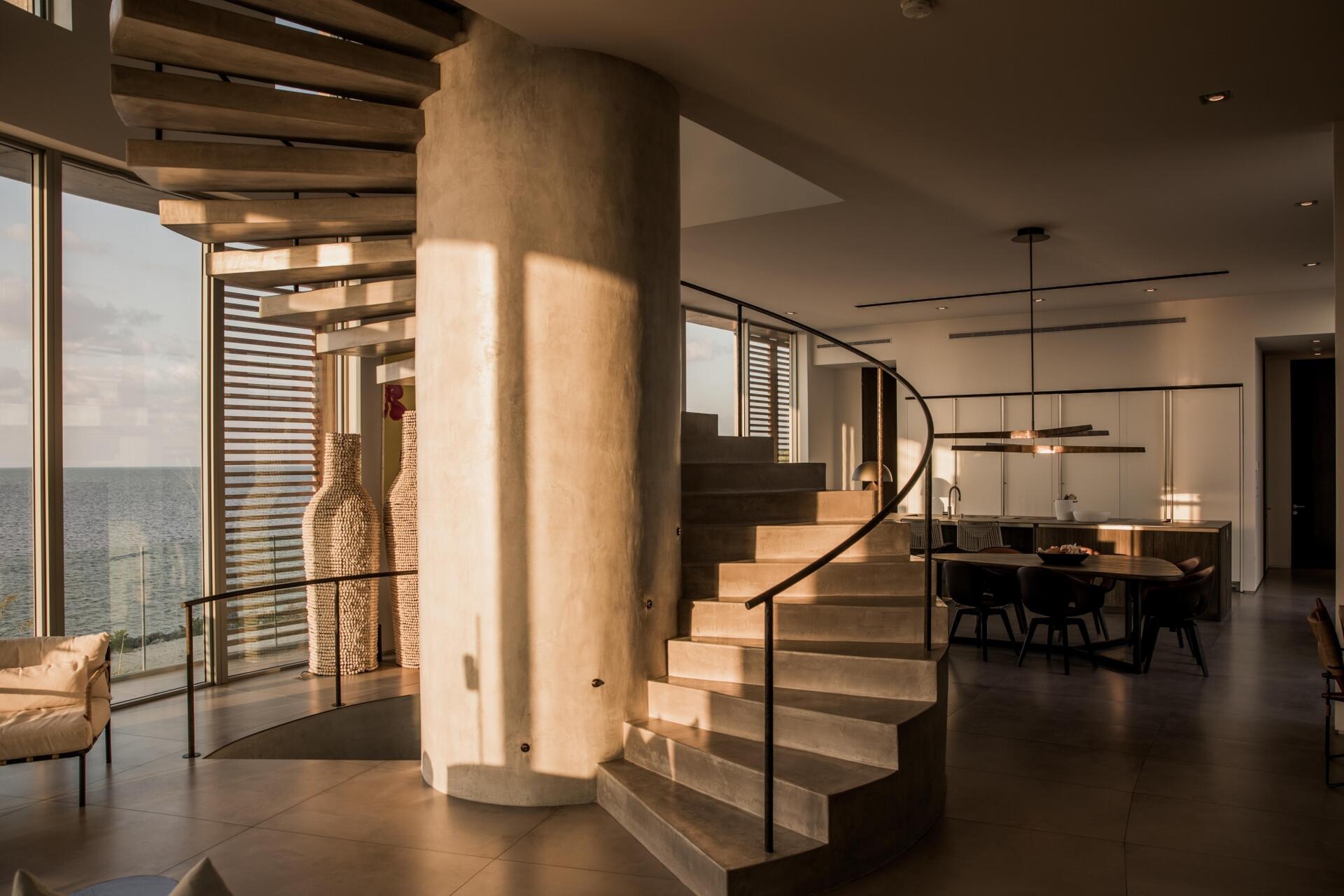 A sculptural spiral staircase in microcement connects the home’s curved geometry to its central axis.