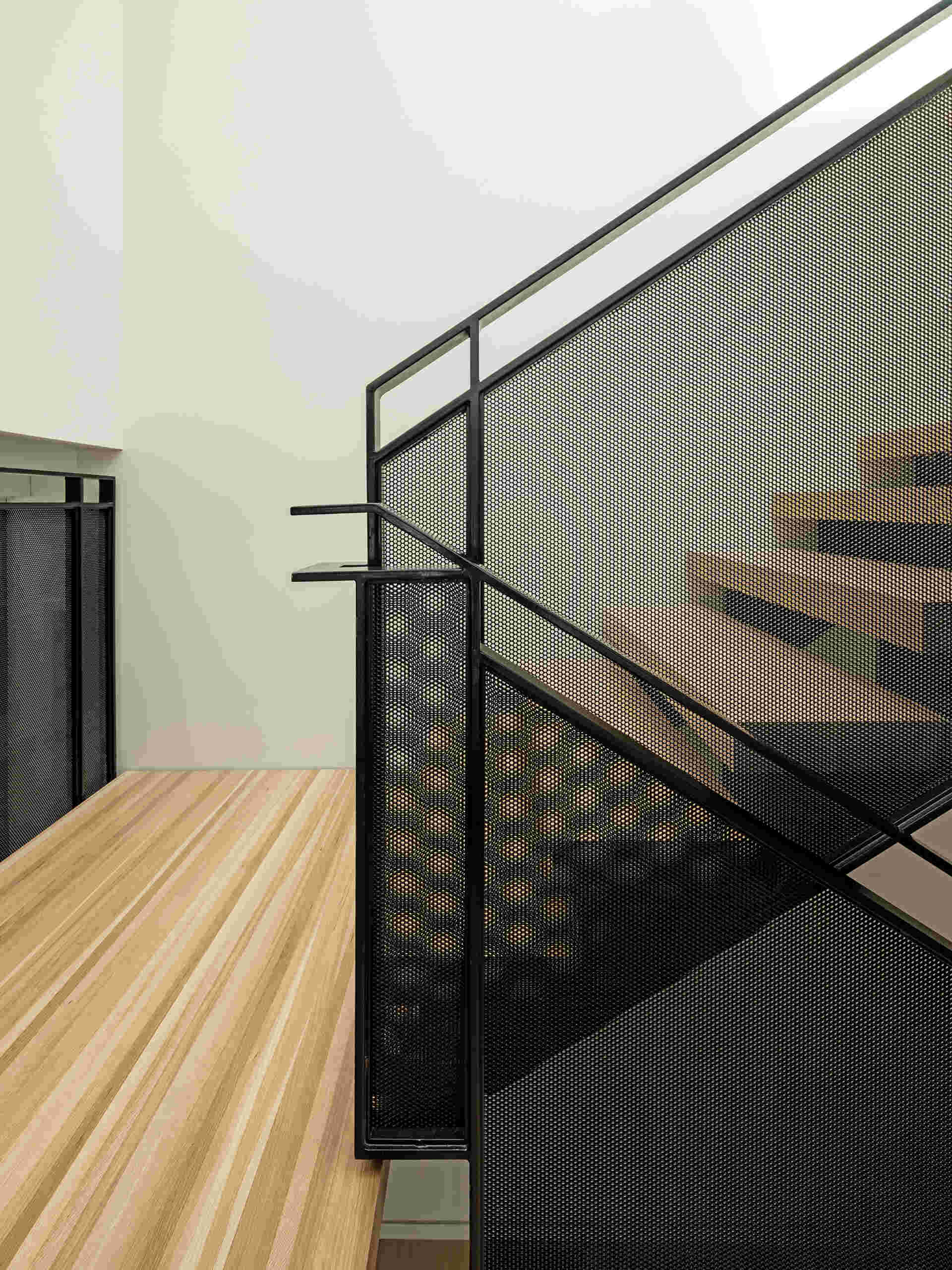 A vertical wood batten screen filters light from a central skylight, animating the stair core with soft, shifting shadows. The staircase connects all levels while continuing the exterior material palette indoors.