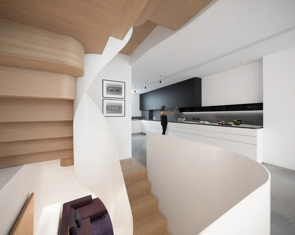 An open plan kitchen, dining, and living space contrasts dark cabinetry with white walls, designed for modern living and art display.