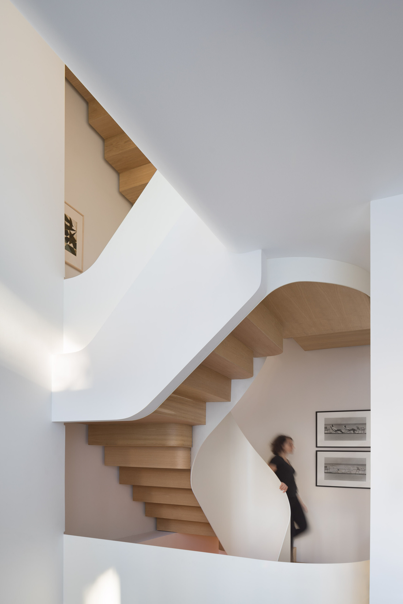 Wood stairs spiral through the home, acting as both circulation and a sculptural centerpiece that connects every level.