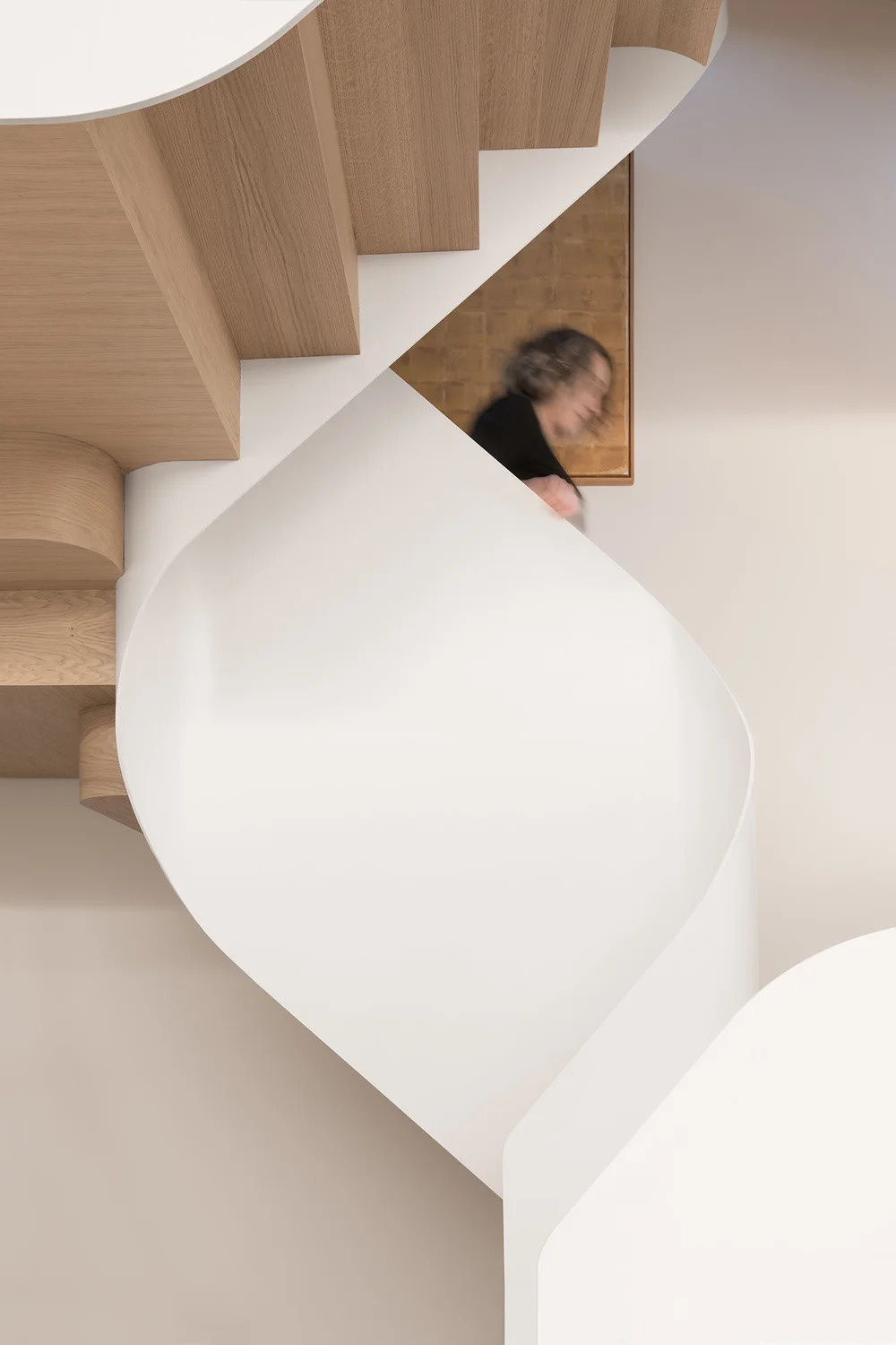 Wood stairs spiral through the home, acting as both circulation and a sculptural centerpiece that connects every level.
