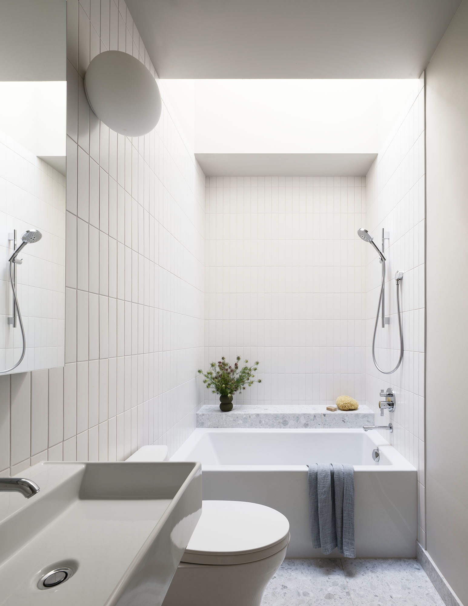 This bathroom pairs a vertical white tiles and a built-in bathtub with an integrated ledge beneath a skylight, turning daily routines into moments of pause. 