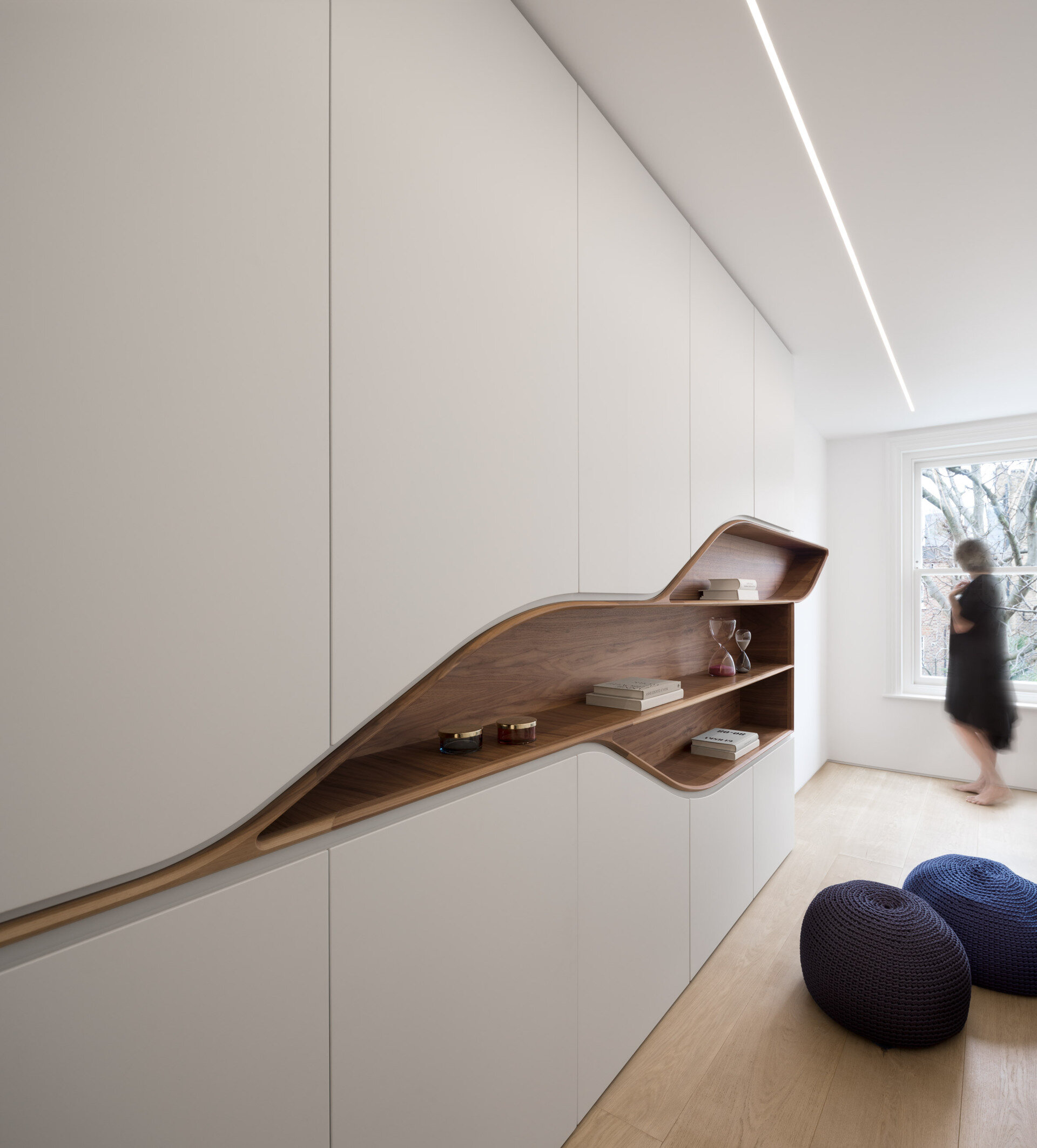 Minimalist white cabinetry frames a curved wood lined shelving feature, blending precision with warmth.