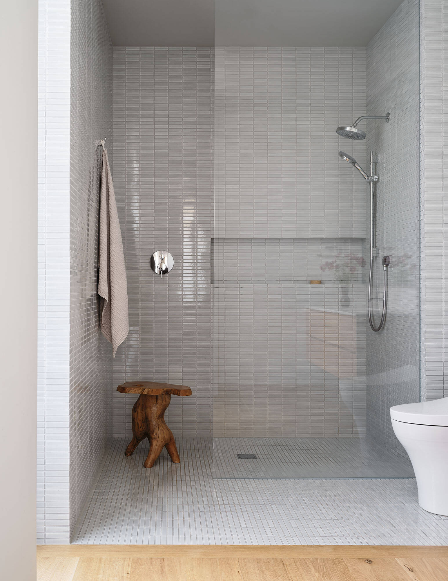 This bathroom has a walk-in shower with small format tile, clear glass, and a timber vanity topped with a pale stone surface.