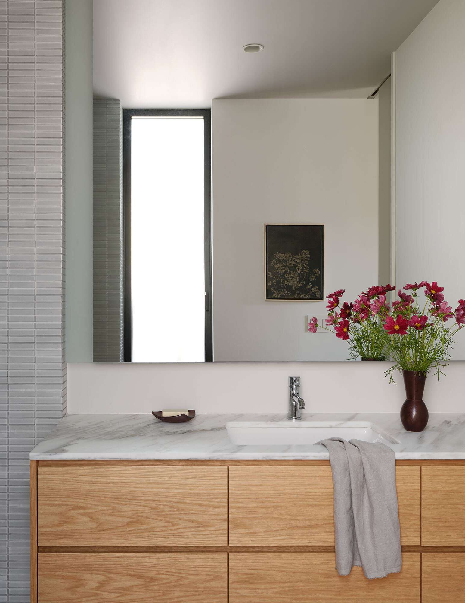 This bathroom has a walk-in shower with small format tile, clear glass, and a timber vanity topped with a pale stone surface.