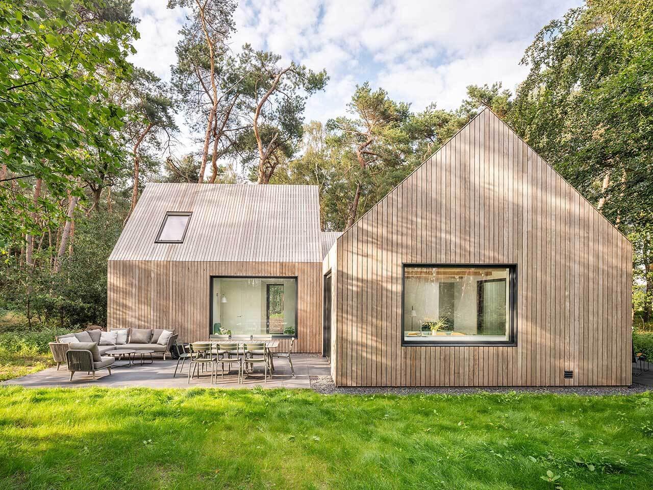 A wood-clad holiday home hidden among the pine trees in Tonden, The Netherlands. Designed with three gabled volumes, this retreat blends into the forest while opening onto peaceful terraces.