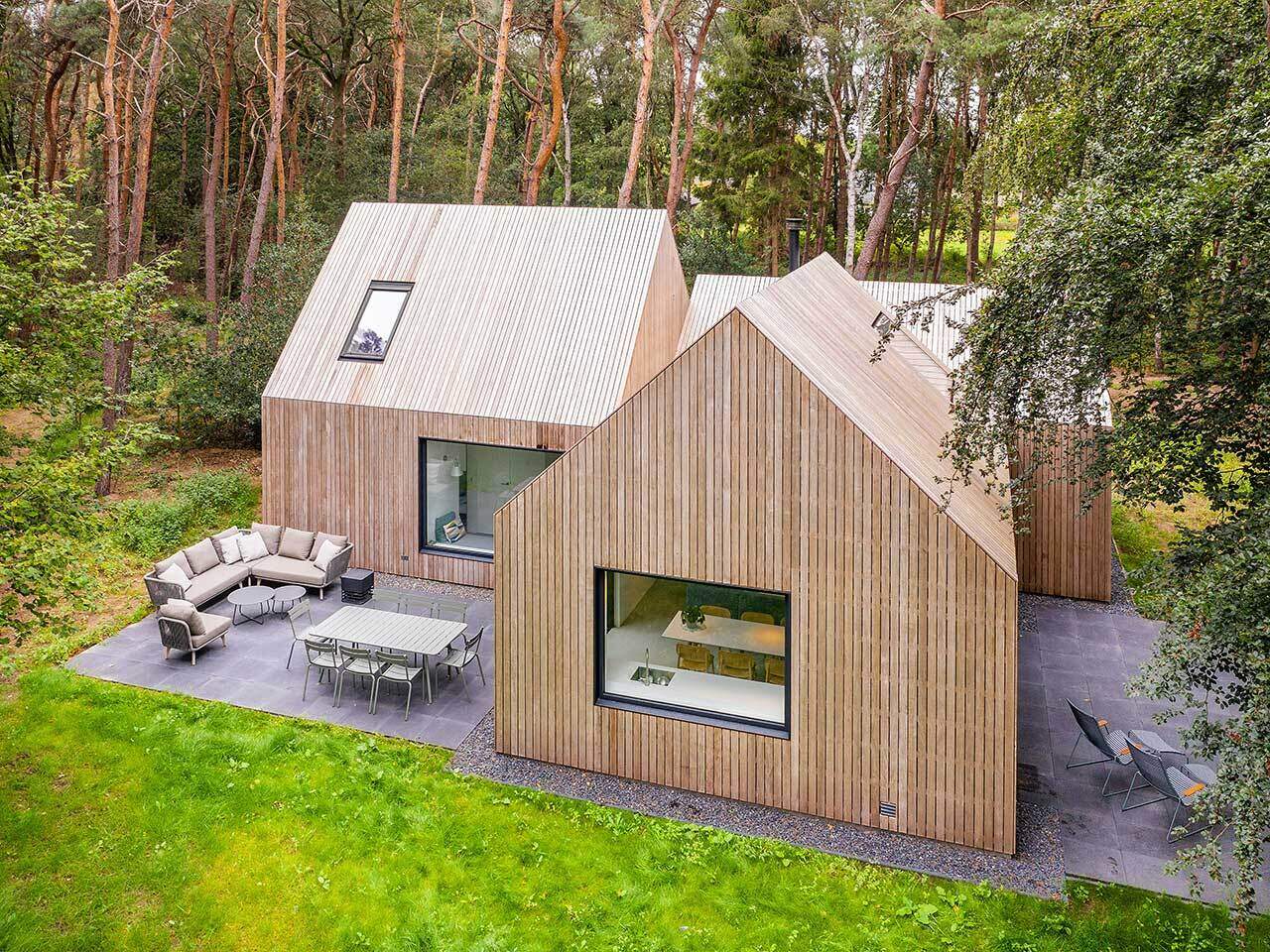 A wood-clad holiday home hidden among the pine trees in Tonden, The Netherlands. Designed with three gabled volumes, this retreat blends into the forest while opening onto peaceful terraces.