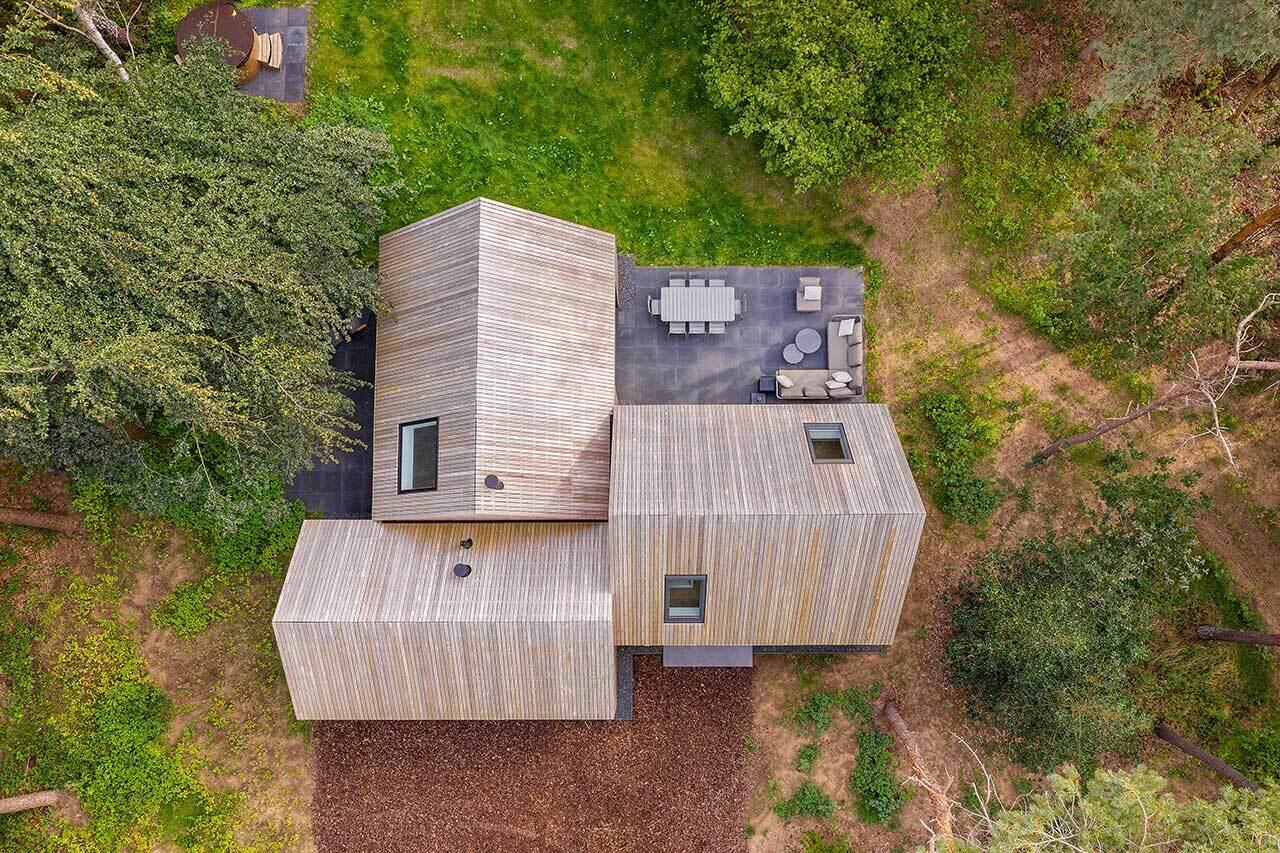 A wood-clad holiday home hidden among the pine trees in Tonden, The Netherlands. Designed with three gabled volumes, this retreat blends into the forest while opening onto peaceful terraces.