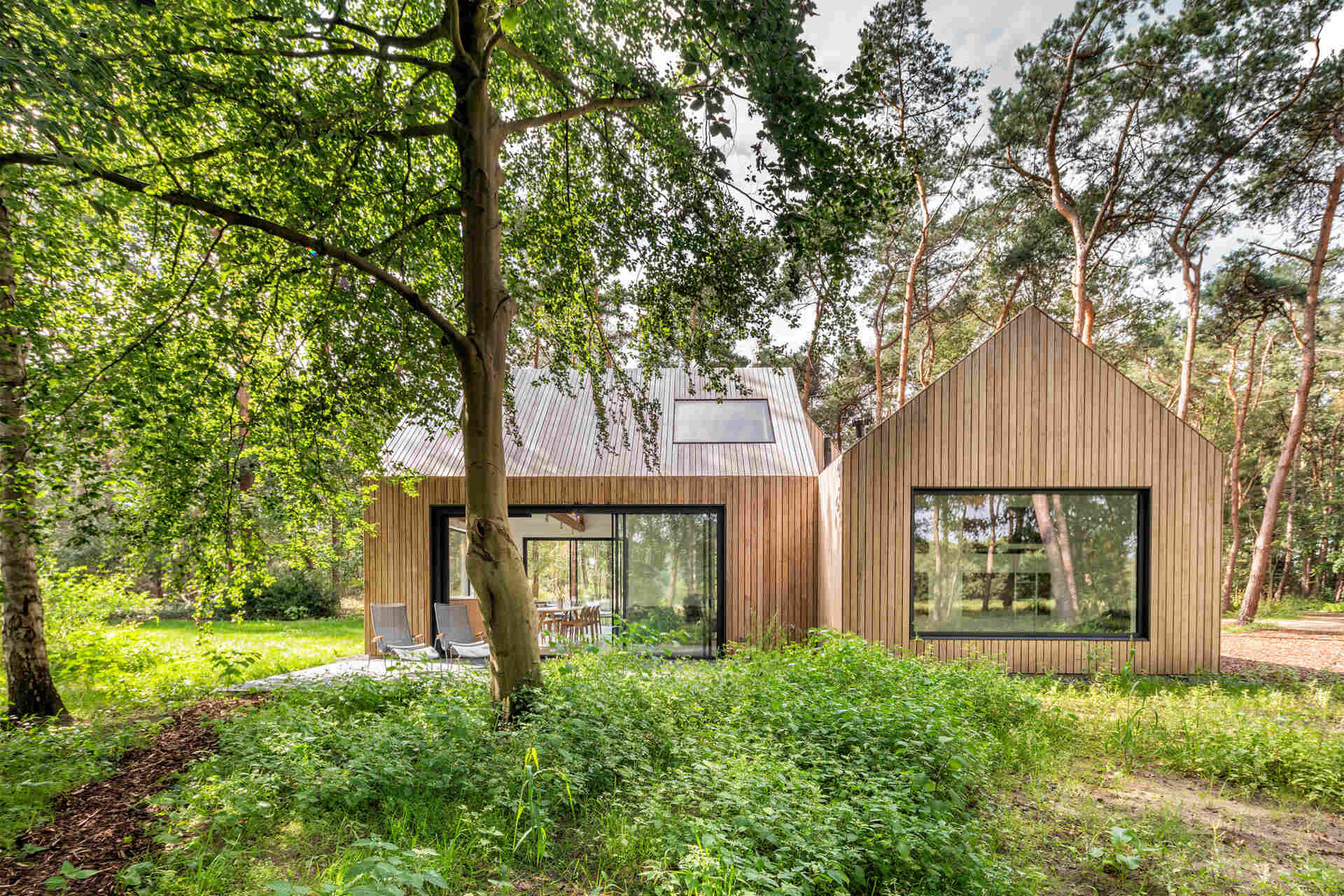 A wood-clad holiday home hidden among the pine trees in Tonden, The Netherlands. Designed with three gabled volumes, this retreat blends into the forest while opening onto peaceful terraces.
