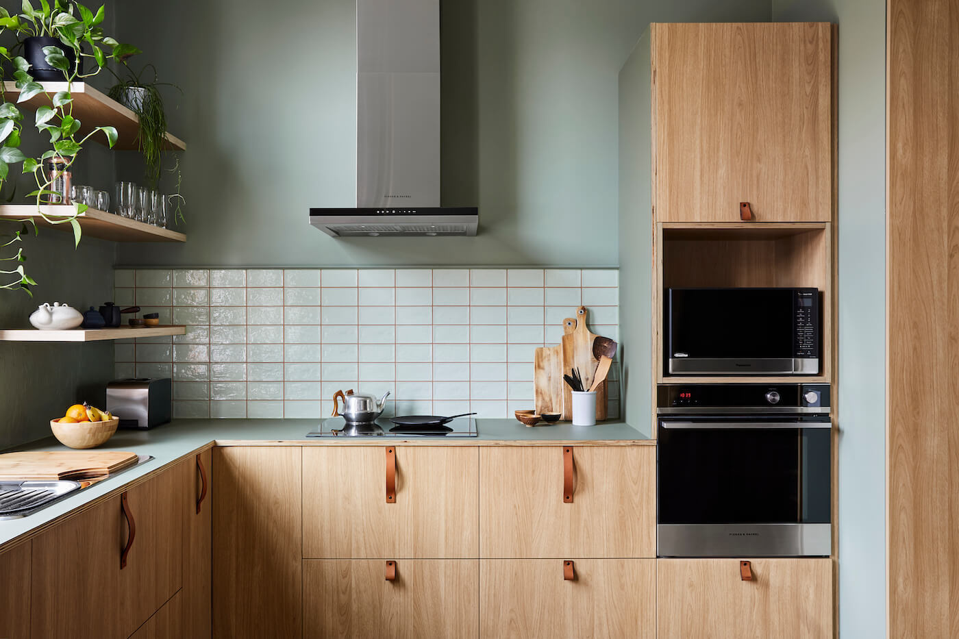 Wood cabinets, leather handles, and sage green walls make the kitchen both practical and stylish.