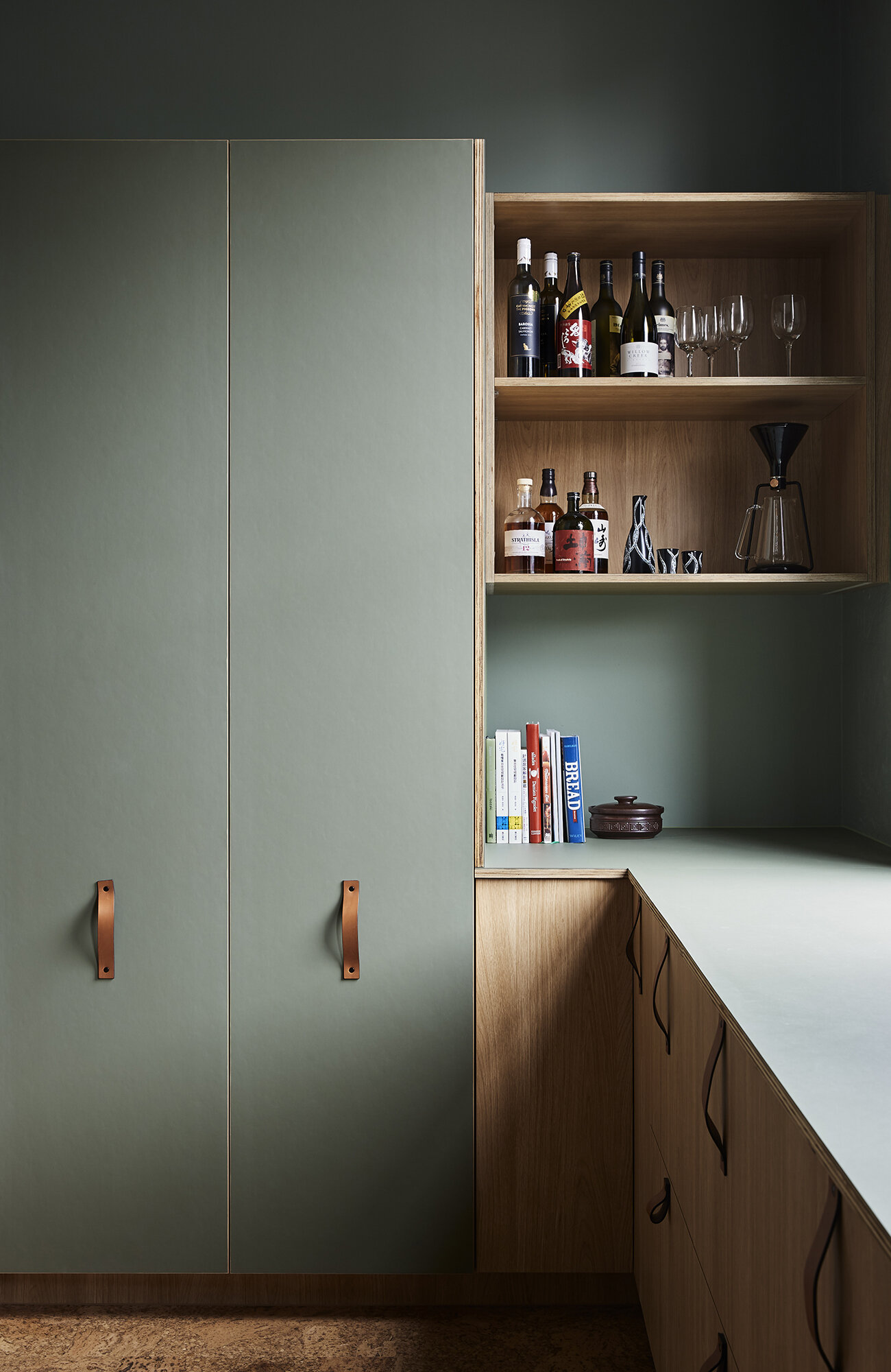 Wood cabinets, leather handles, and sage green walls make the kitchen both practical and stylish.