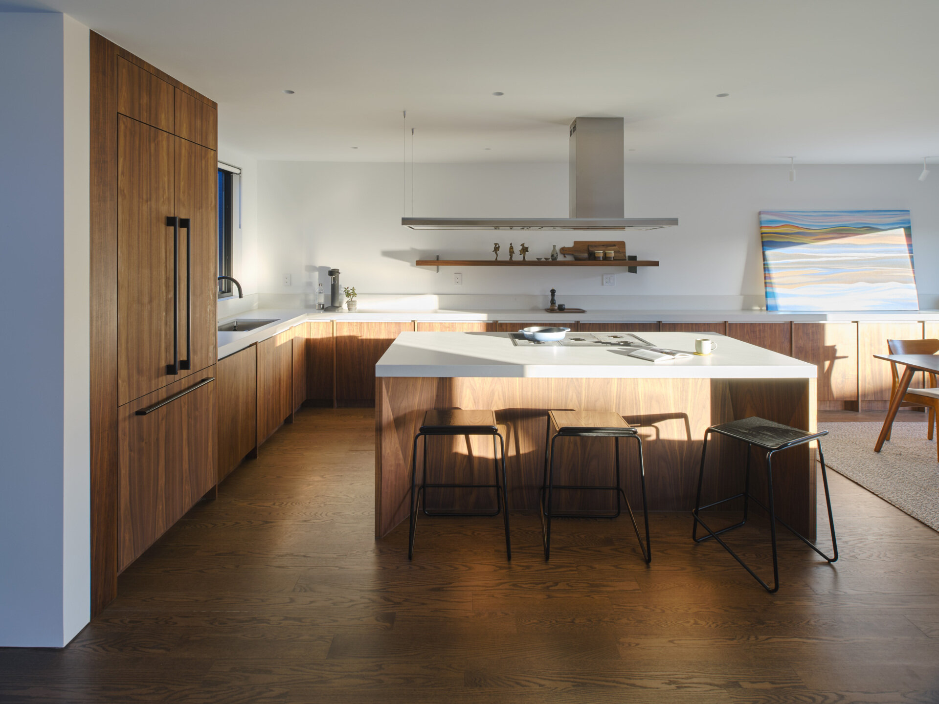 Before, the kitchen was part of the home’s dark and divided interior, lacking a strong relationship to the rest of the living spaces. After the renovation, the kitchen becomes a focal point. A walnut clad island folds geometrically upon itself, inspired by the home’s original 45 degree angled walls.